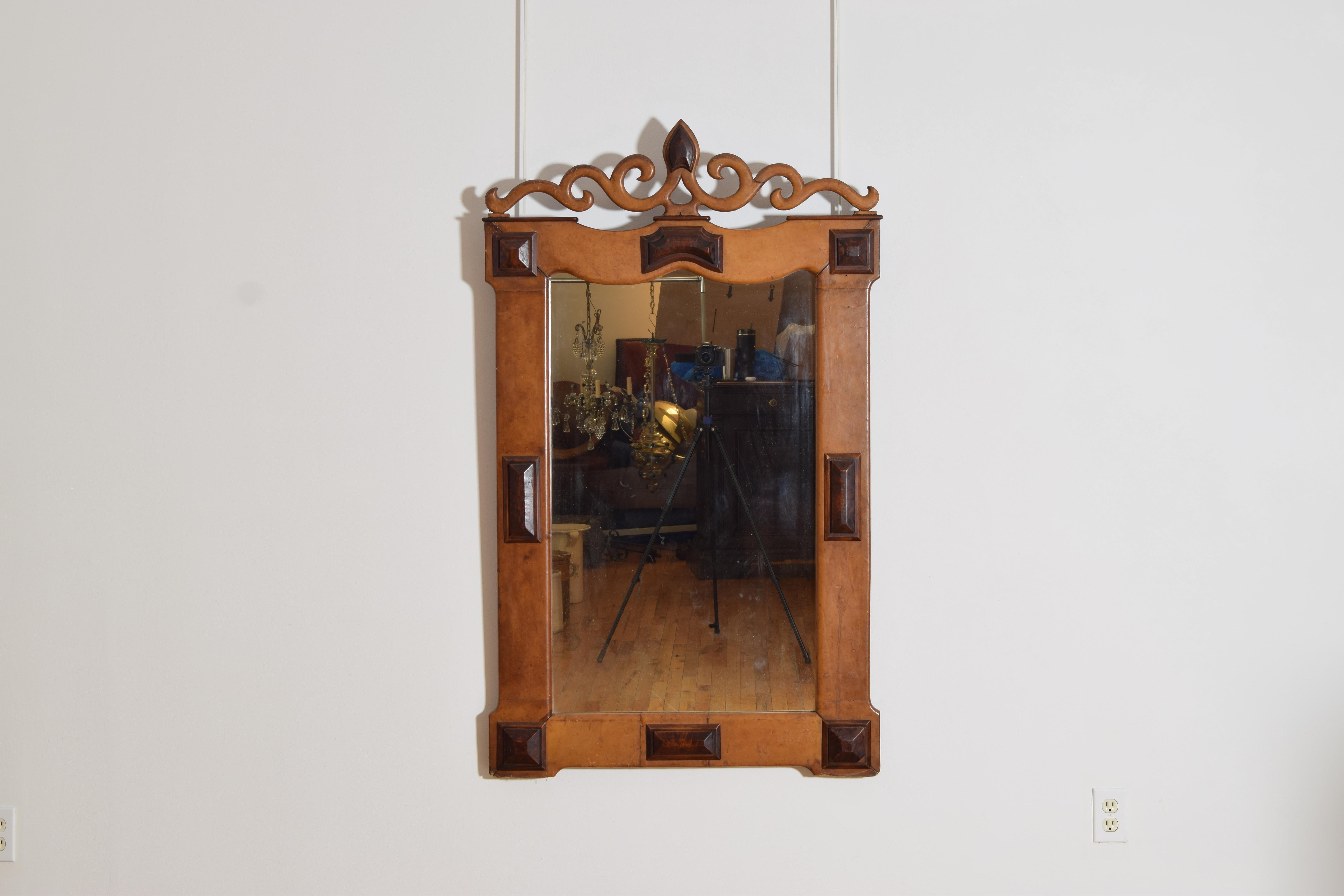 de style baroque, ce miroir unique est entièrement recouvert de deux tons de cuir différents, avec des éléments décoratifs façonnés dans les coins et sur les côtés, le sommet étant orné d'un fleuron décoratif en forme de volute.