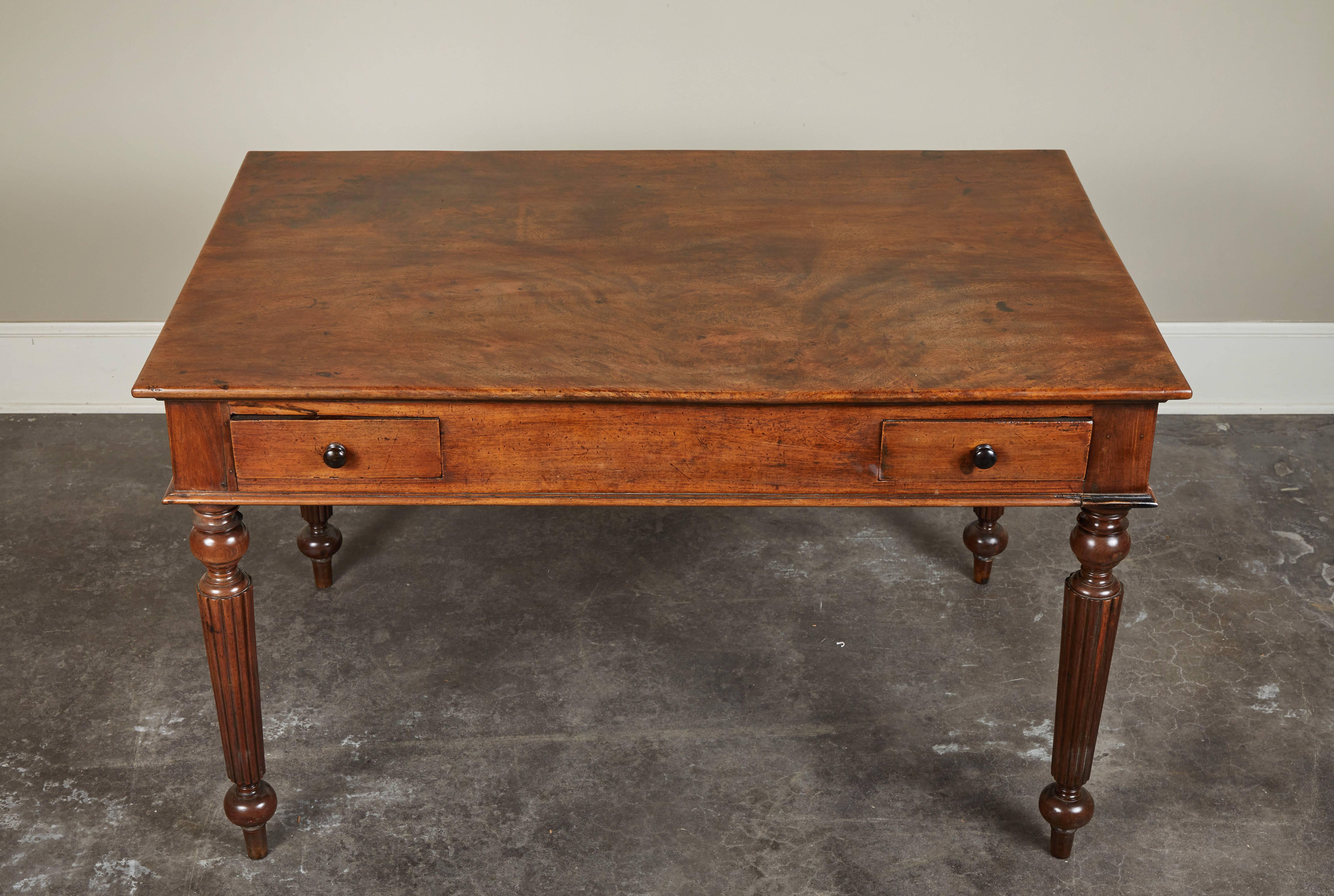 A great petite French Colonial rosewood desk. Top is one single piece of rosewood, with two small drawers on simple reeded and turned legs. Timeless and functional.