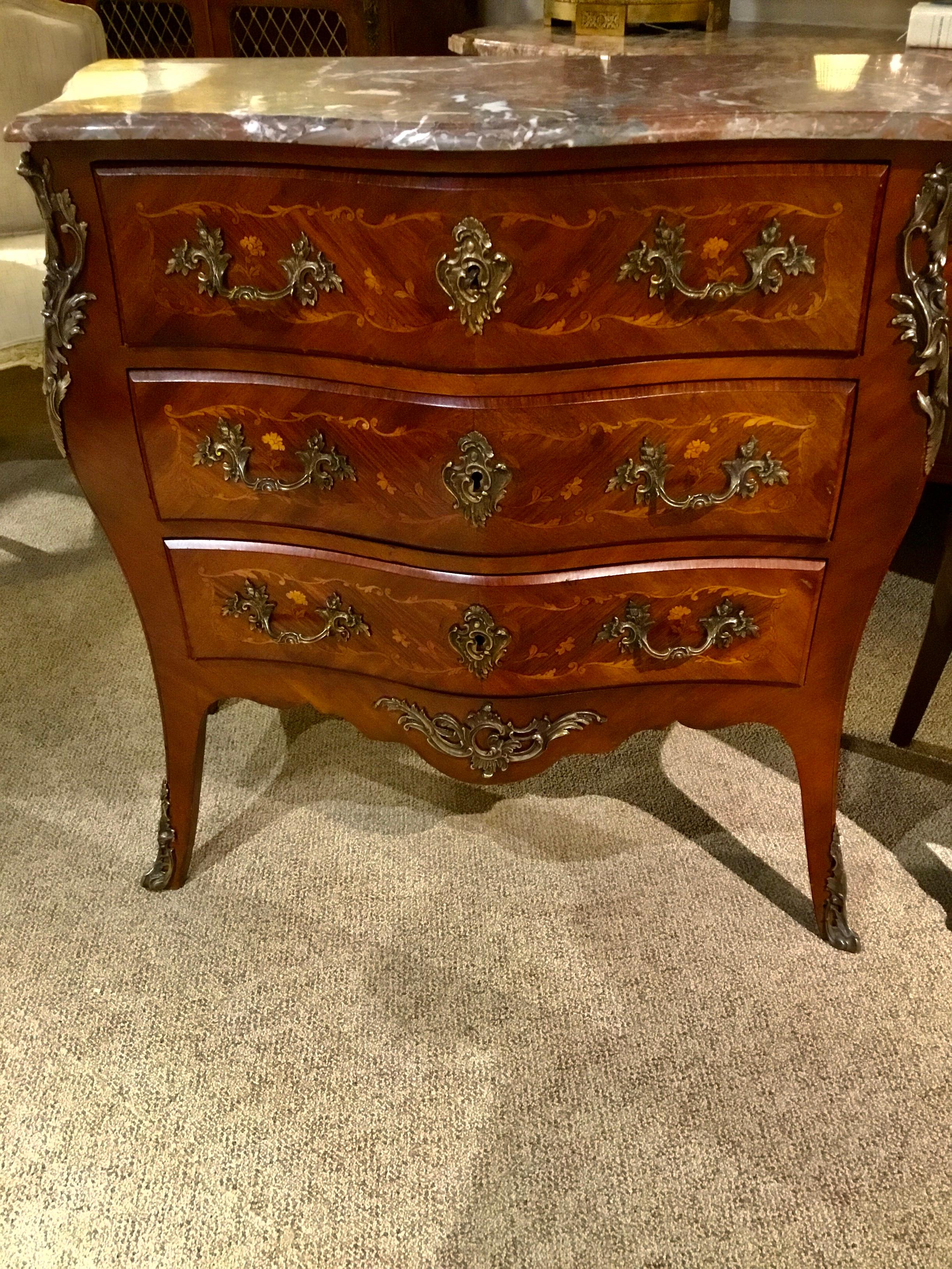 Rouge marble top commode/chest of drawers having three drawers. Intricate floral marquetry inlay in
Satinwood and tulipwood. Bronze mounts on front corner and at center bottom. Sabots are mounted
At the feet. Original bronze handles and key holes.