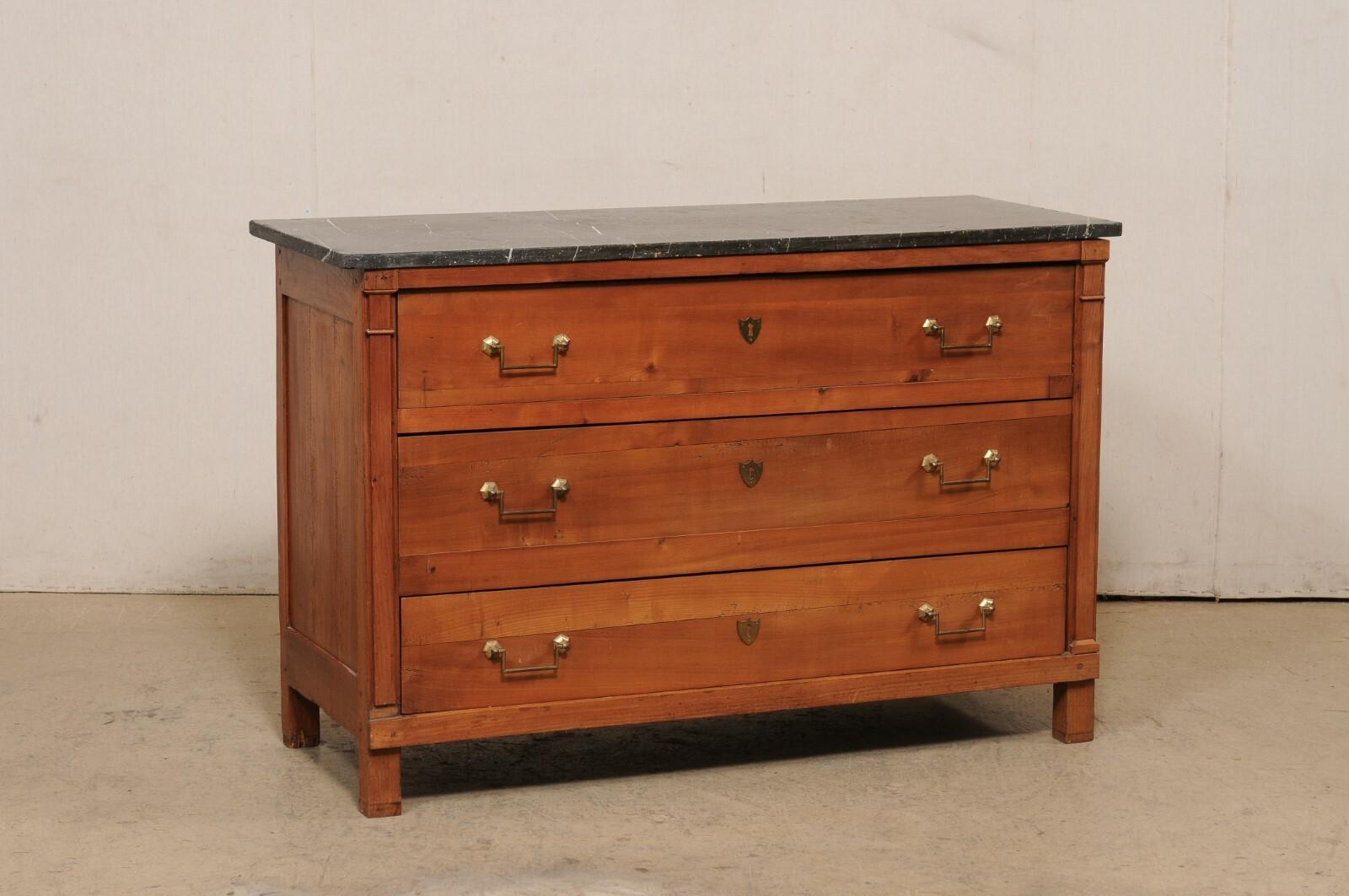 A French Neoclassical chest of drawers, with marble top, from the 19th century. This antique commode from France features a rectangular-shaped black marble top, which rests atop a case that houses three full size graduated drawers, set within