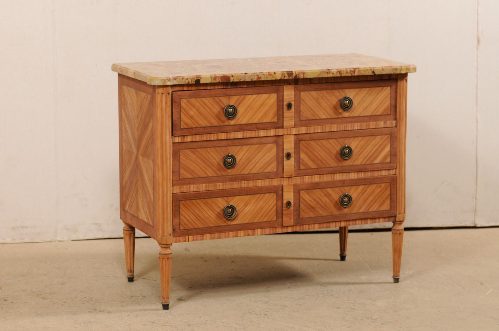 A French commode on legs with stone top from the early 20th century. This antique chest from France features a stone, likely scagliola, top with rounded, cove-edges at both front corners, atop a neoclassical-style case with rounded and flute-carved