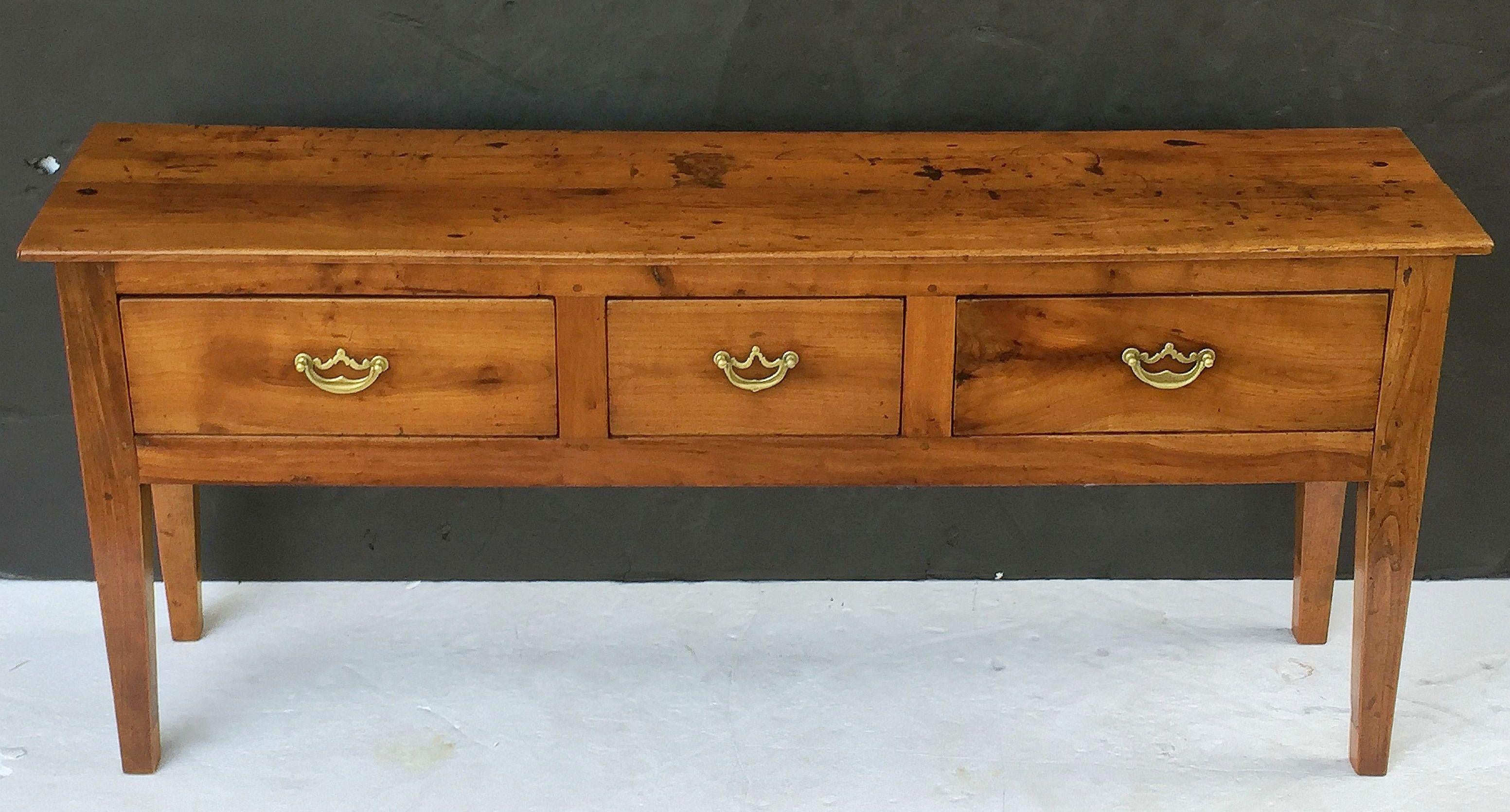 A handsome French console sideboard (or serving table) of cherrywood featuring a rectangular plank top over a large frieze with three drawers, each with brass hardware pulls, panelled back and sides, and resting on tapering square legs.