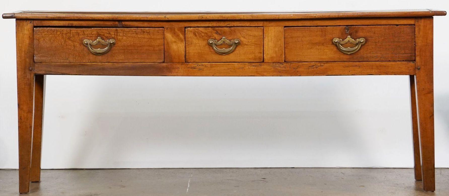 A handsome French console sideboard (or serving table) of patinated cherrywood, featuring a rectangular plank top over a frieze with three drawers, each with brass hardware pulls, paneled back and sides, and resting on tapering square legs.