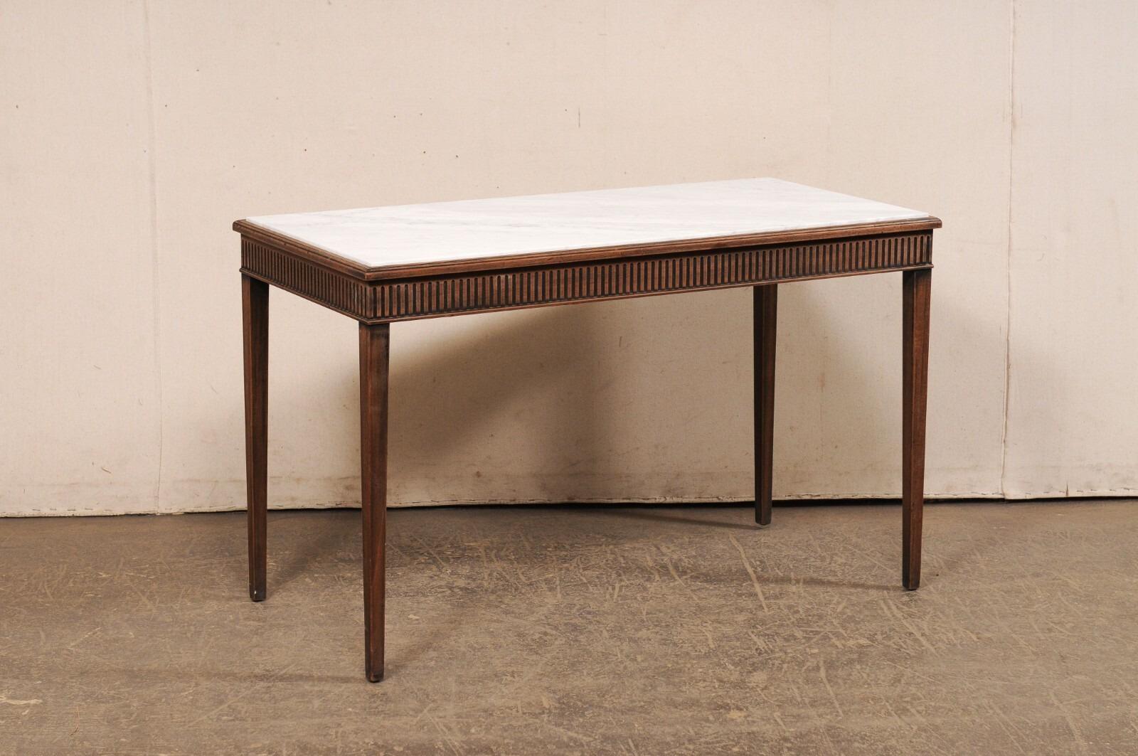 A French carved-wood console table, with honed marble top, from the mid 20th century. This vintage table from France features a rectangular-shaped honed-marble top (a newer addition to the piece) which is recessed within a linear molded wood