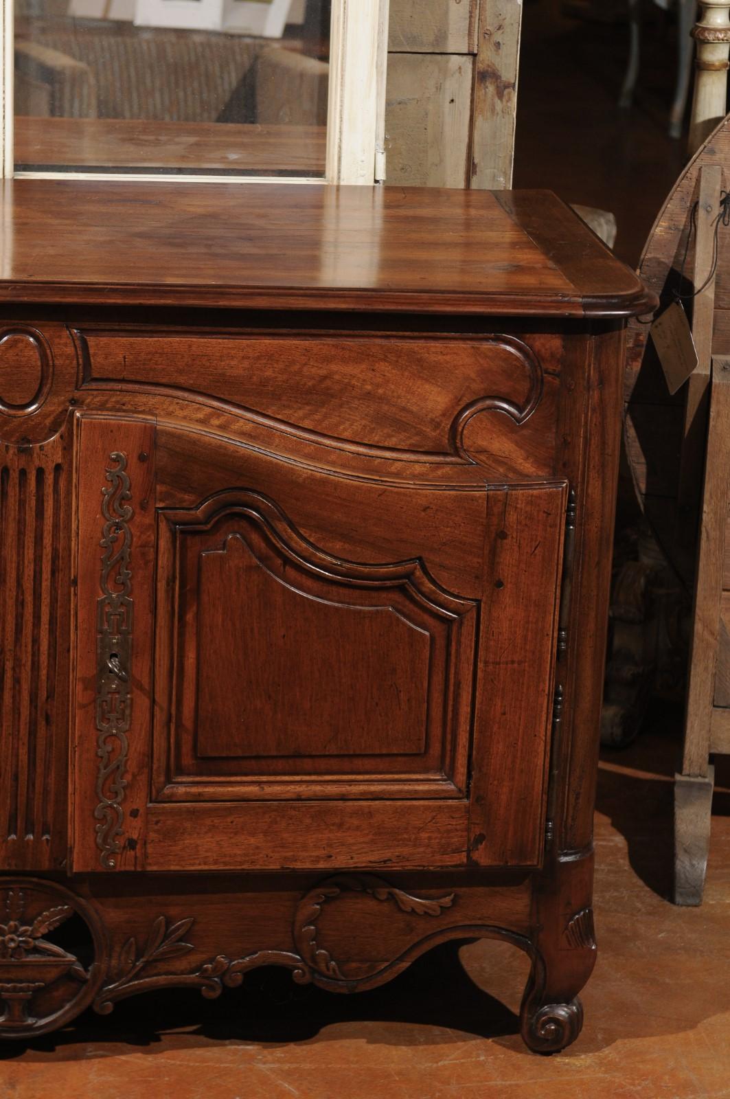 A French walnut buffet from the early 19th century, with hand carved foliage and urn motifs. Born in France during the Consulate period that witnessed the emerging presence of Napoléon Bonaparte as First Consul, this exquisite two-door buffet