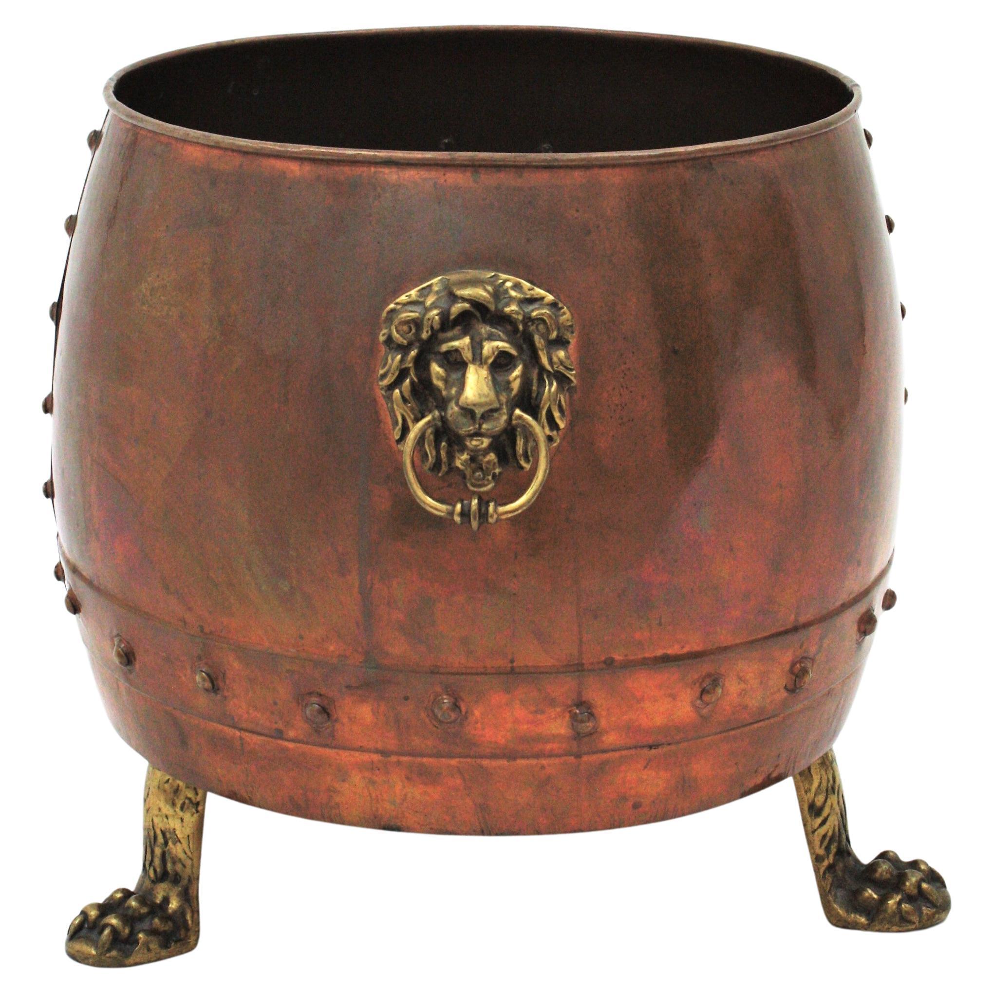 Large French copper and bronze cachepot / jardiniere or log bin with lions head handles and tripod paw feet. 
This hand-hammered copper cauldron has copper studs and it has a terrific aged patina. It is supported by tripod paw feet. At both sides it