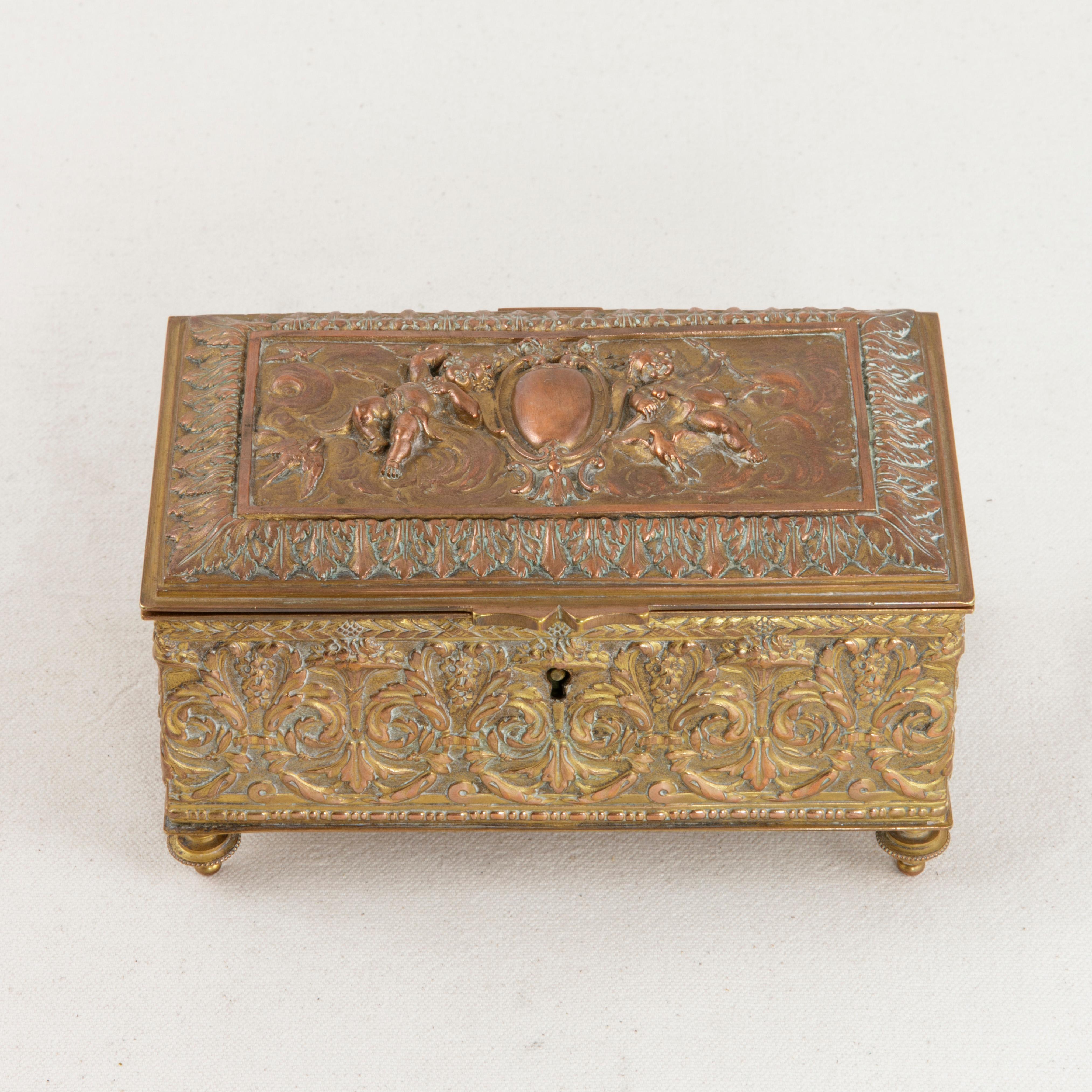 This French copper box with lid from the turn of the 20th century features a repousse facade detailed with an intricately scrolled acanthus leaf pattern. The lid is decorated with a central cartouche flanked by cherubs and birds. The box rests on