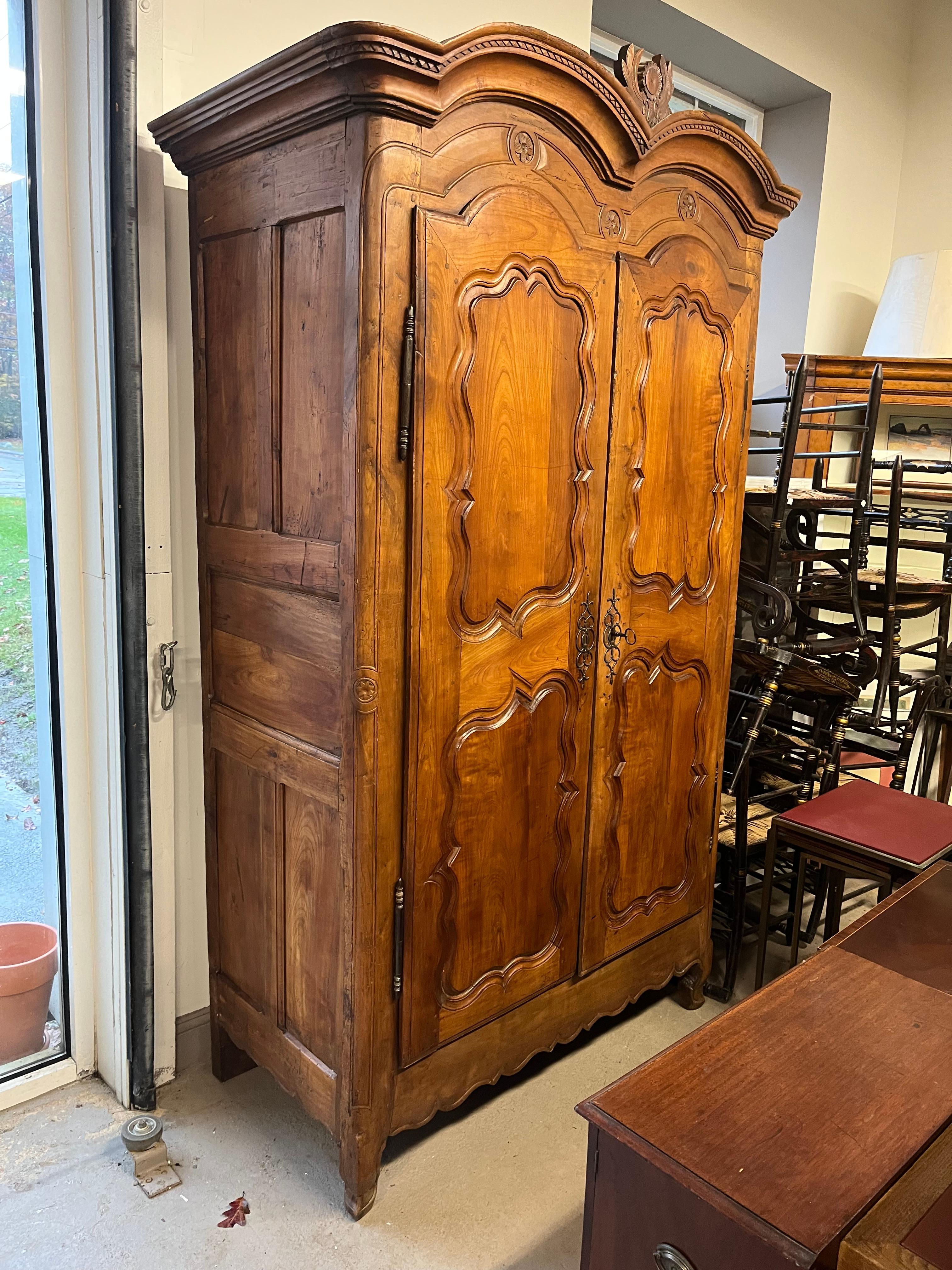 An impressive Louis XV period “double bonnet” armoire in wild cherry from the Brittany region of France. The 2 doors are carved with inset panels and floral motifs. The double crown has a carved sunflower bouquet with stylized leaves between the two