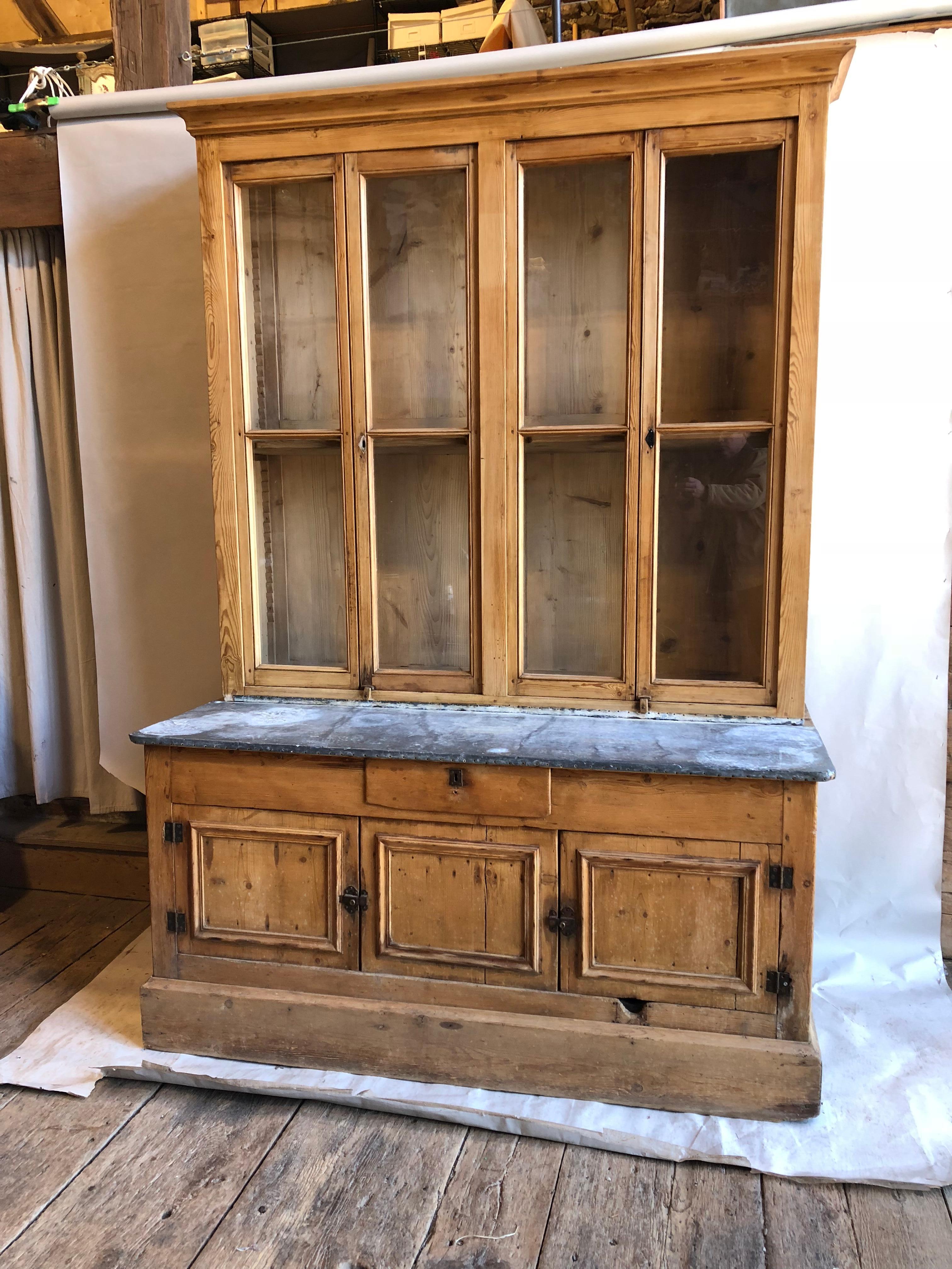 A French country kitchen cabinet in 2 parts, in stripped pine with glazed doors and a zinc work surface, late 18th century. Four glazed doors with adjustable shelves in upper cabinet which rests on a zinc-top lower cabinet with drawer and lower