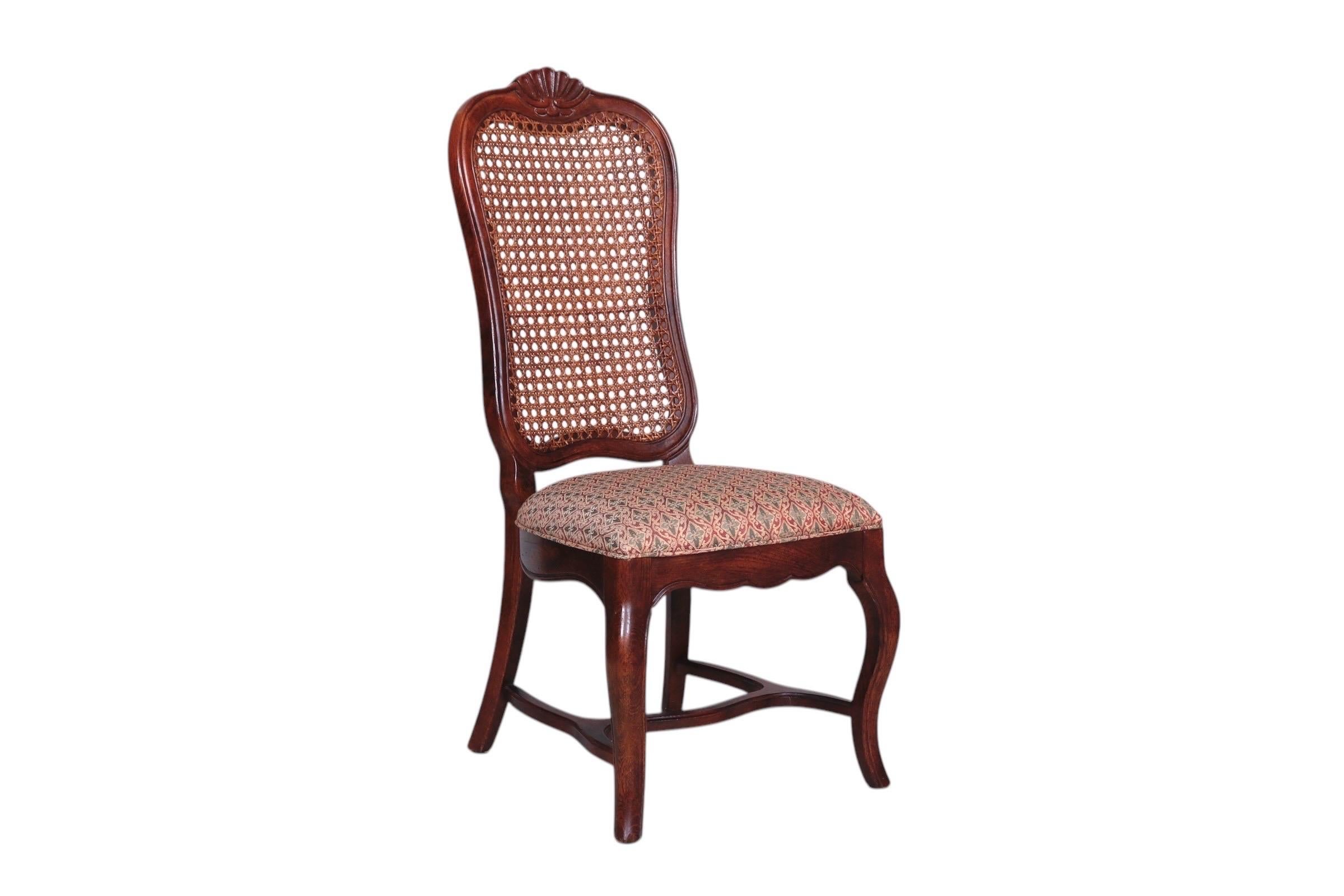 A set of six French Country style dining chairs. Tall, caned seat backs are decorated with carved shell details on the crest rails. Two armchairs have outward flared arms that terminate in scrolled hand holds. Tight seats are upholstered in a