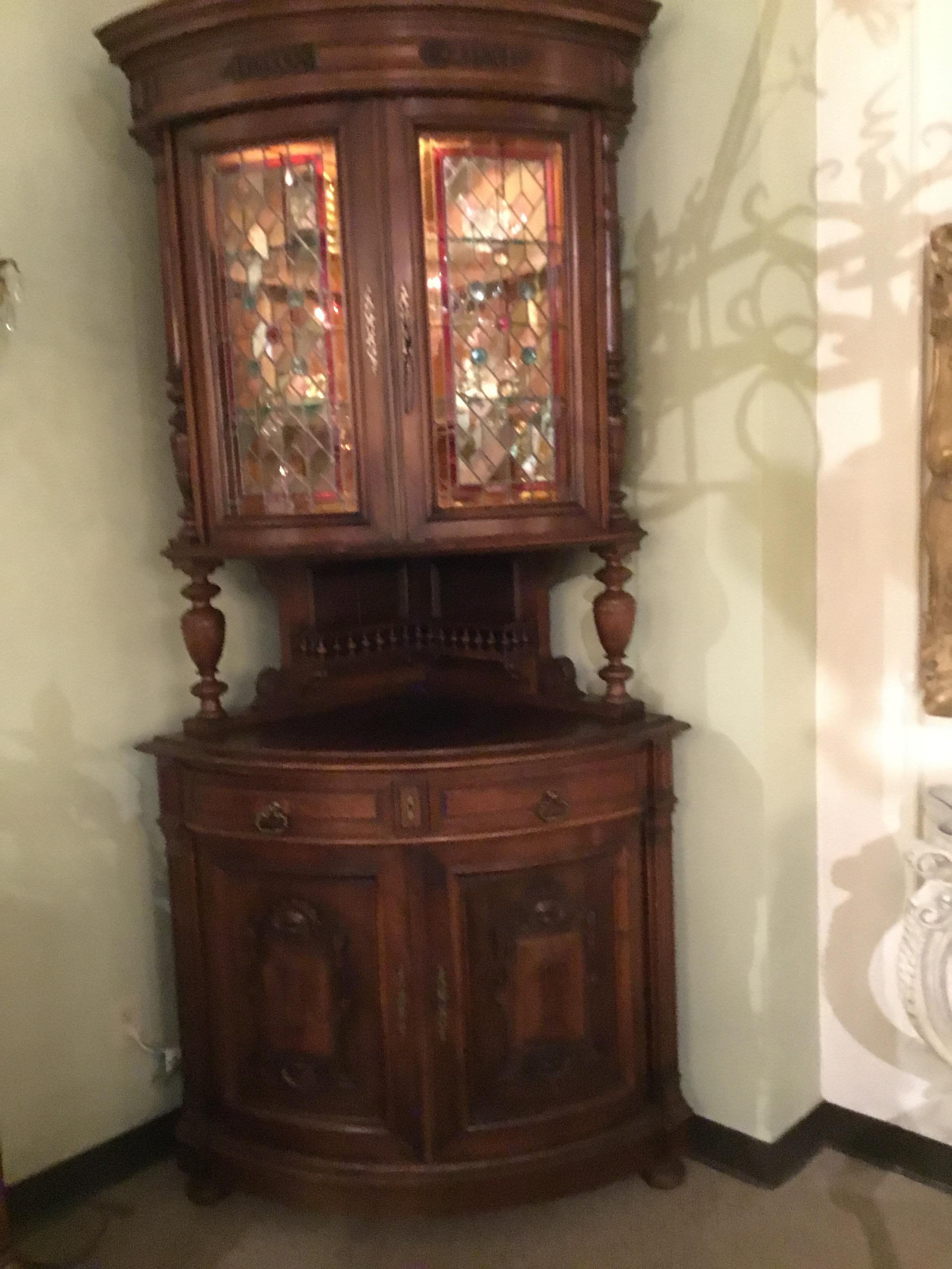 Handsome corner cabinet with two stained glass doors above a lower
cabinet that has two drawers and two doors below.. The upper structure
is supported by turned posts. Two glass shelves are in the upper structure.