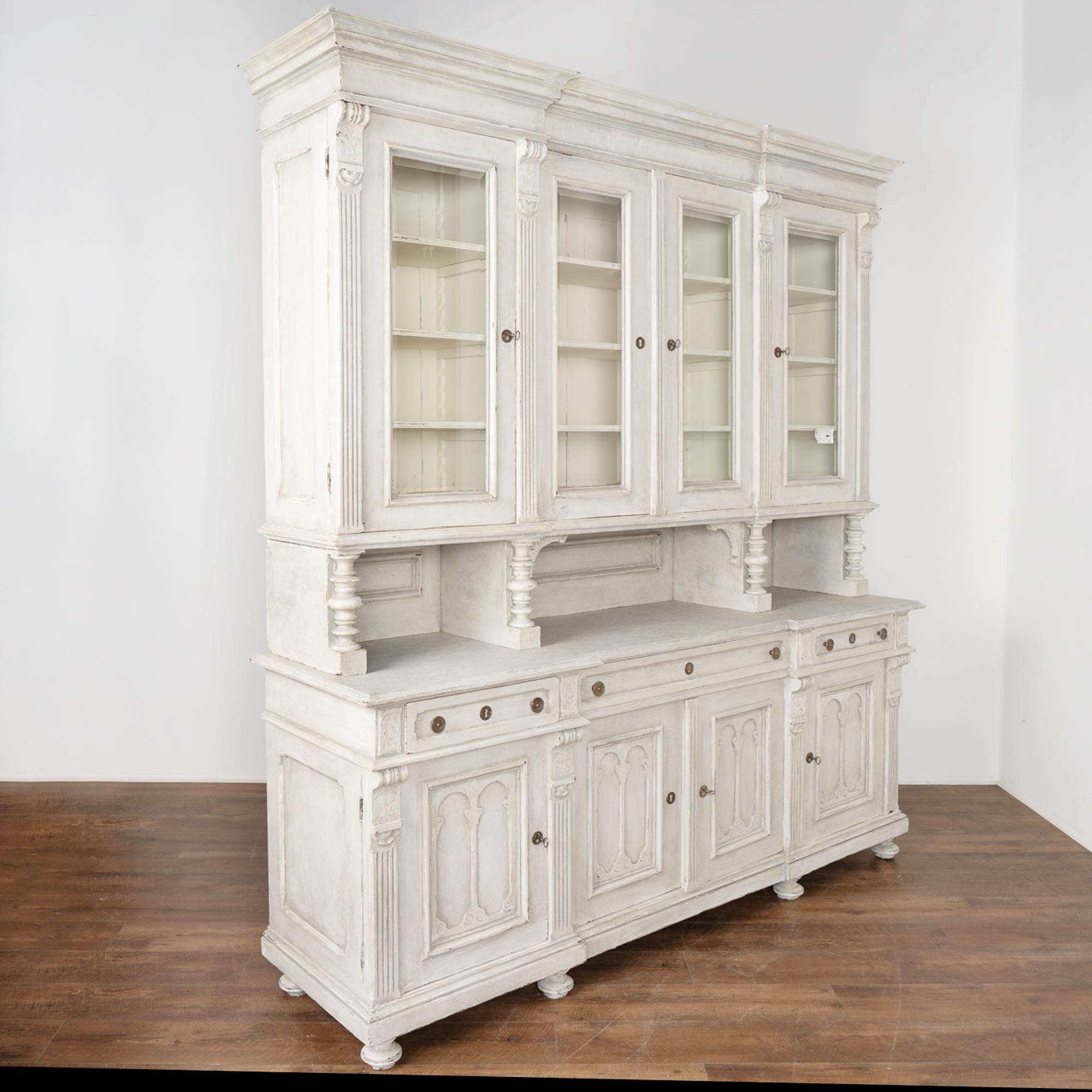 French country large display cabinet or bookcase in two sections.
Oak wood later professionally painted in layers of white and light grey with softly distressed finish fitting the age and grace of this stately cabinet.
Enlarge photos to appreciate