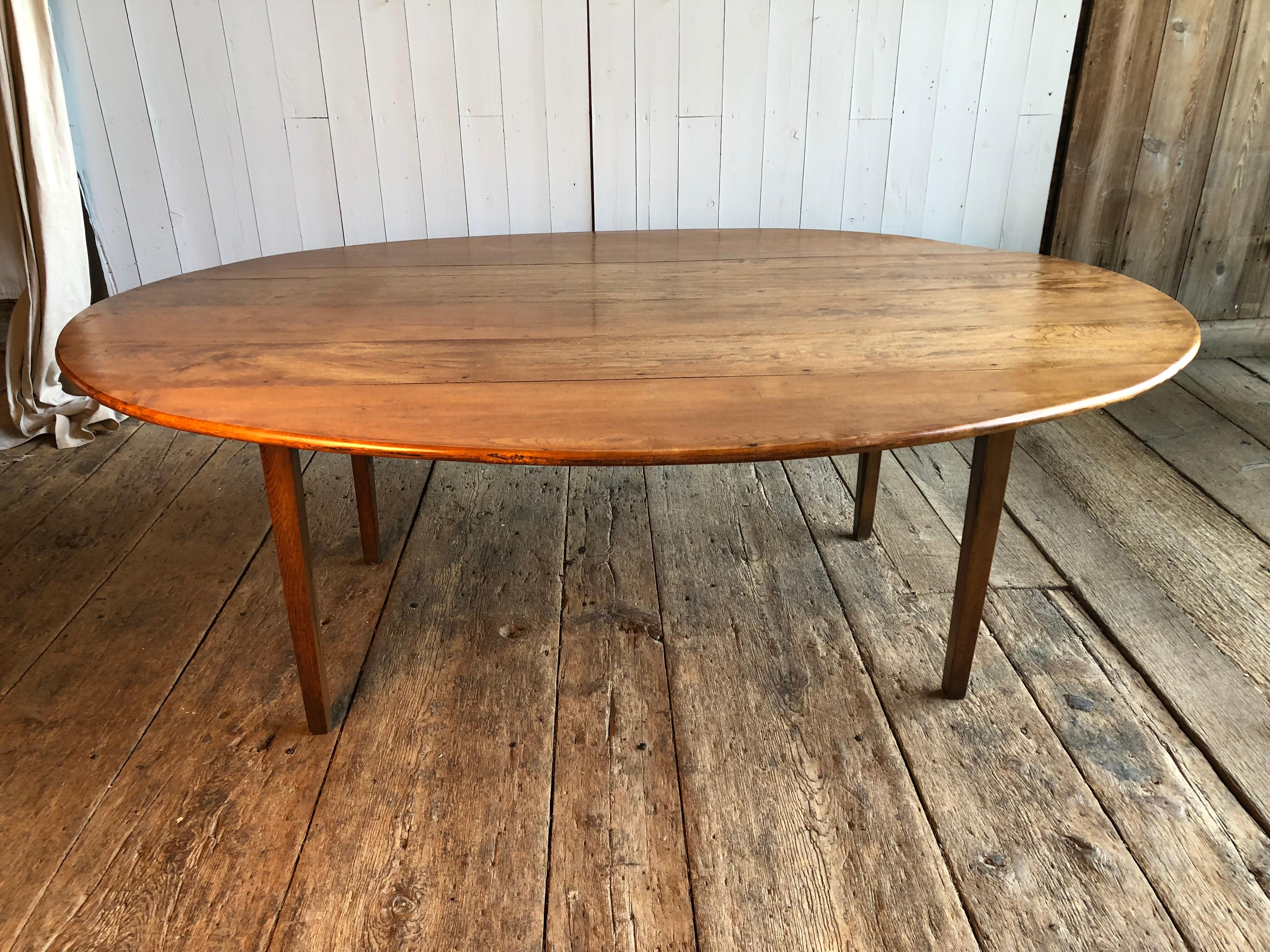 A large oval French country farm table, in fruitwood colored oak, with simple tapered square legs, and a large drawer on one end, late 19th-early 20th century.