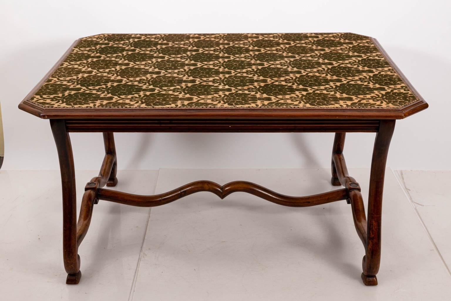Walnut library table in the French country style, circa early 20th century. The piece also features upholstered top in antique Grillage while the fabric is in the William Morris style with nail head trim. The base also features scrolled legs and