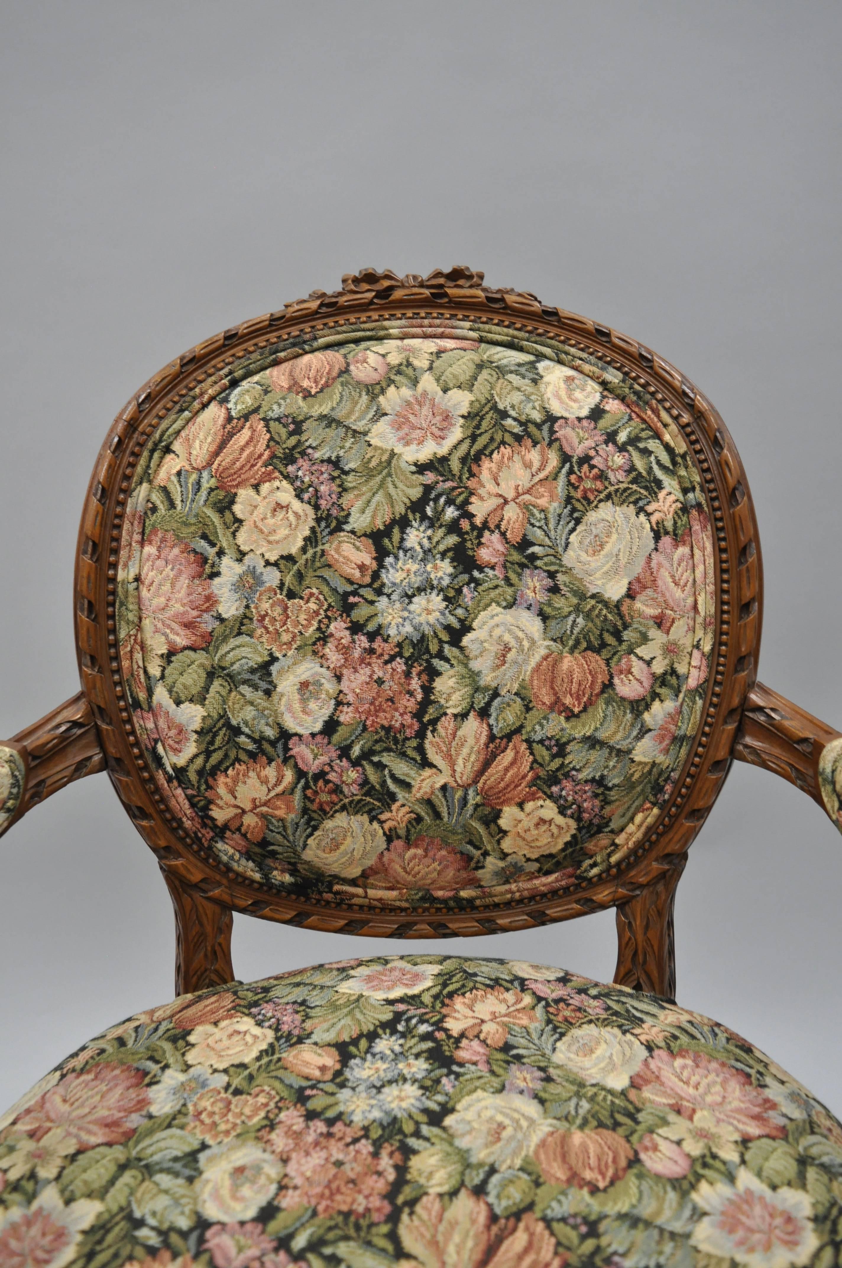 Pair of Early 20th Century French Country / Louis XV Style Finely Carved Walnut Armchairs with Round Backs. Chairs features ornately carved solid wood frames, cabriole legs, ribbon carved crests, carved round backs, and floral upholstered fabric.