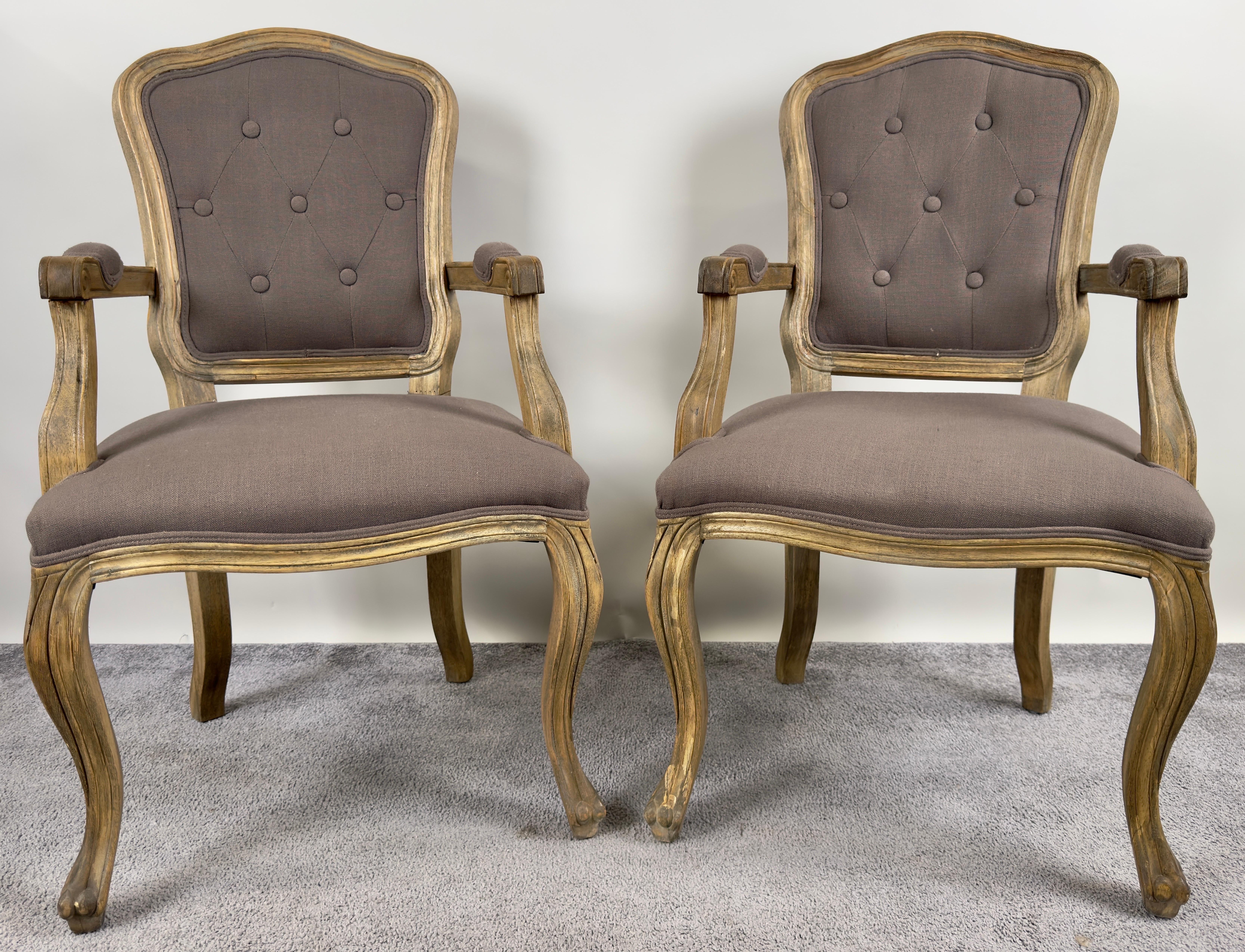 This elegant pair of French country Louis XV-style bergère chairs evokes a timeless sophistication with their classic form and luxurious upholstery. The frames, crafted from weathered wood with a patina reminiscent of aged oak, showcase the