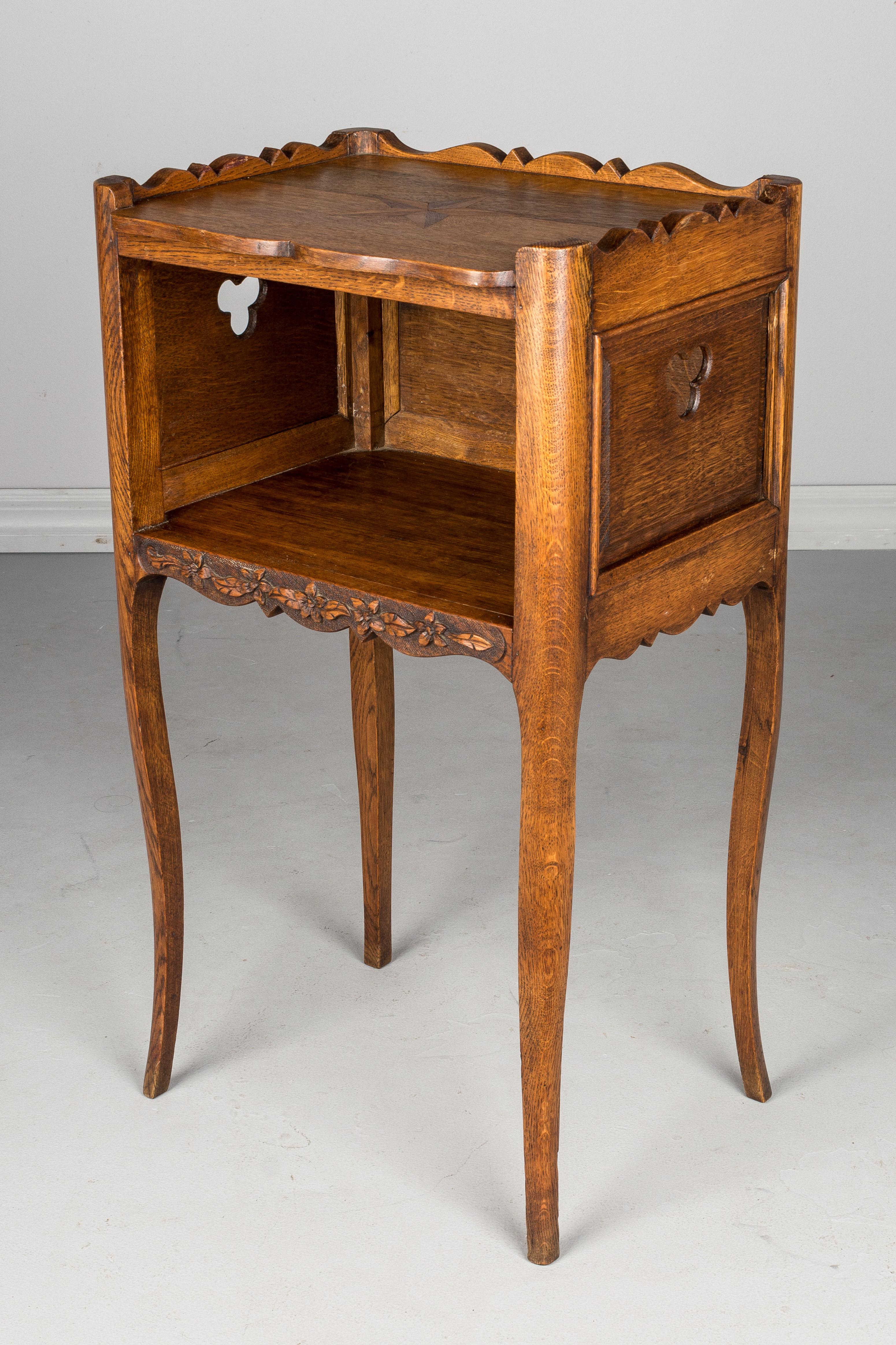 A Louis XV style country French side table or nightstand made of solid oak, with pierced clover shaped cut-outs on the on the sides and hand carved floral decoration. Marquetry star on the top surrounded by a scalloped gallery. Slender curved legs.