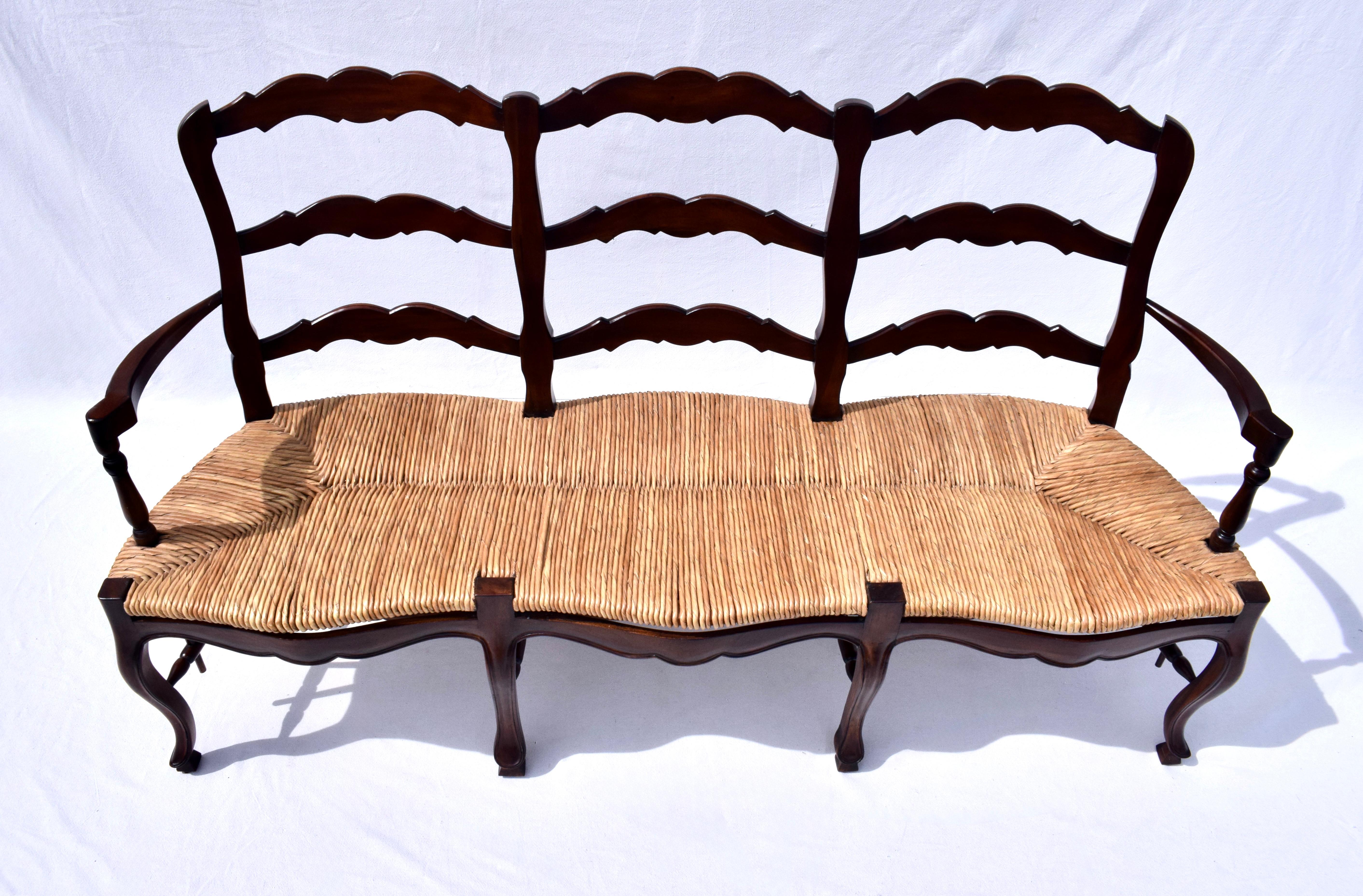 Banc français classique à dossier en échelle, en acajou, avec trois sièges en jonc tissé à la main et une triple traverse à la base. Les gracieux pieds cabriole et les pieds en sabot sculptés offrent un magnifique aspect rustique qui évoque la