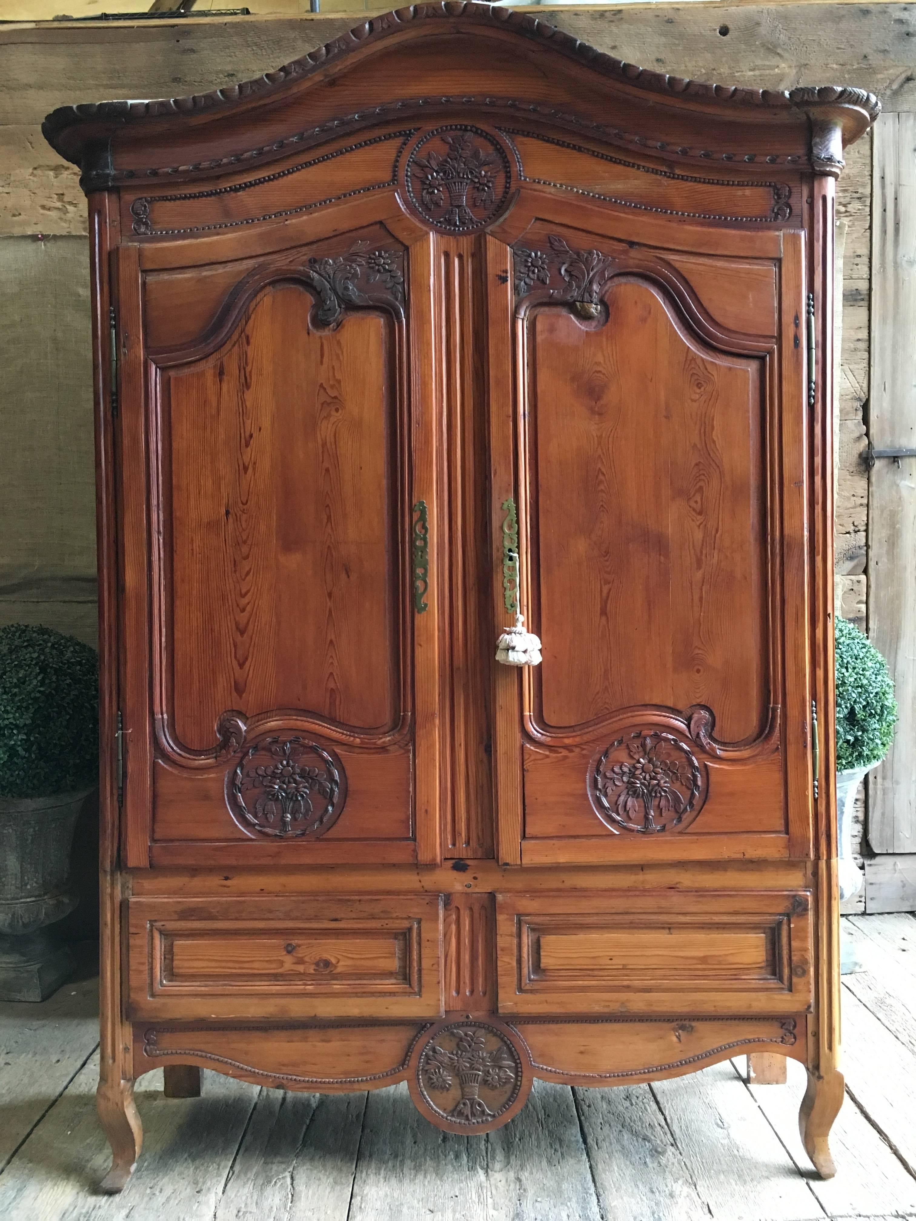 A petite Louis XV pine wedding armoire from Normandy France, circa 1800, with an arched cornice over two doors, nicely carved with bouquets of flowers etc., over two drawers, all on cabriole legs. There is a label on the interior of one door from