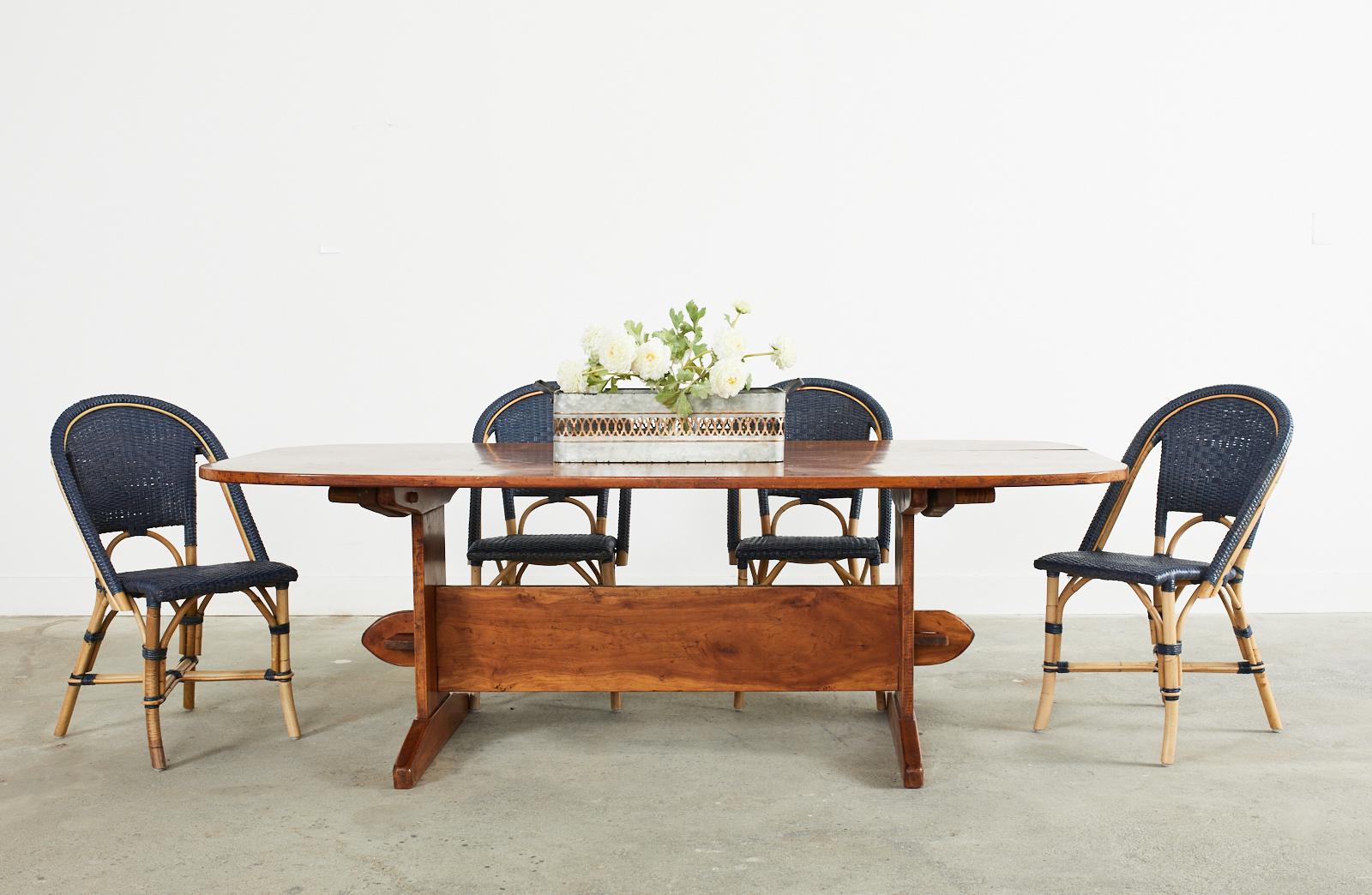 Gorgeous early 20th century French country farmhouse dining or harvest table crafted from fruitwood. The table features an oval plank top supported by a trestle style base with a large, exposed mortise and tenon joinery. The straight legs are