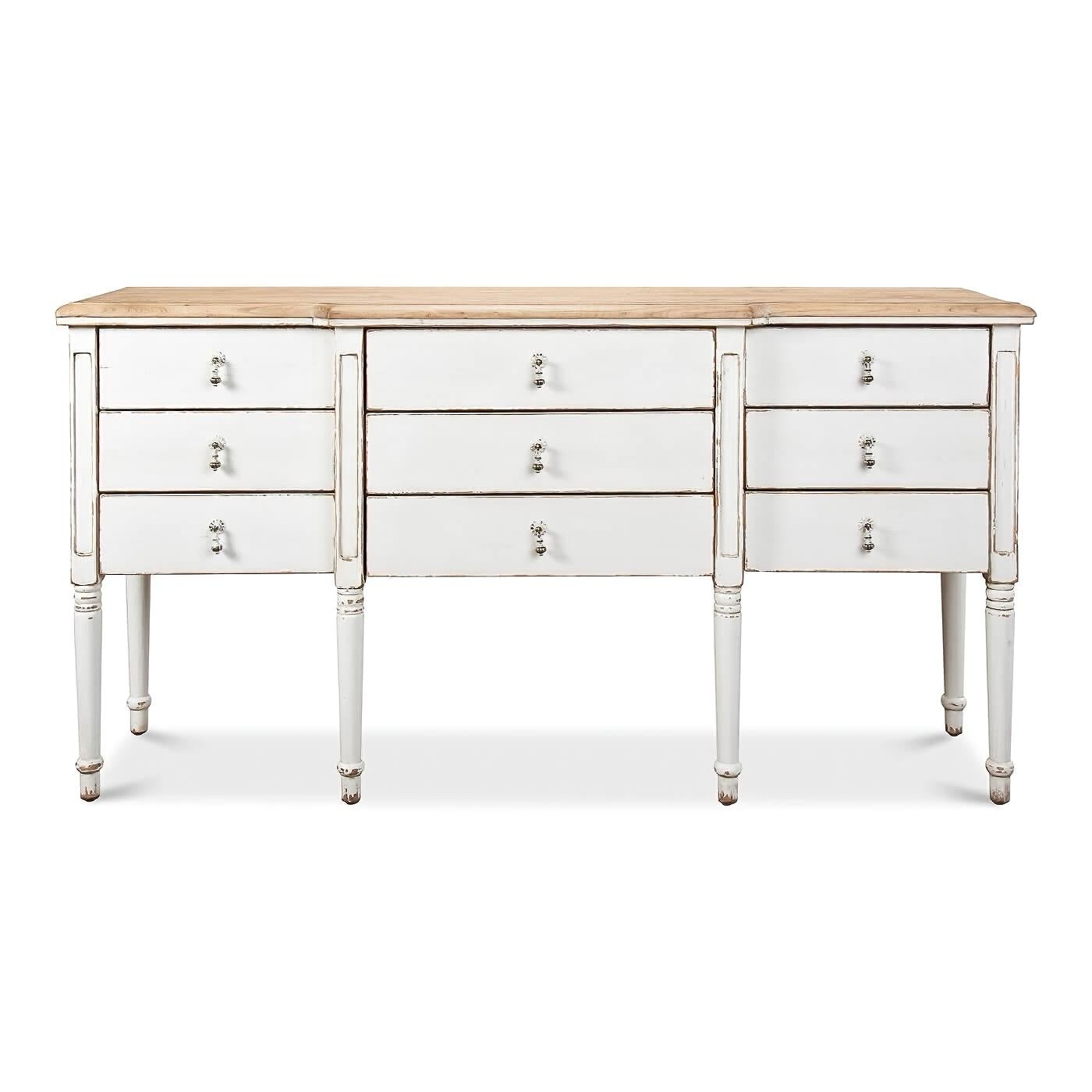 A French Country painted sideboard with a whitewash finish and a natural pine top. Inspired by a French country antique, this sideboard has nine individual drawers with decorative drop pulls. The lower cabinet has a distressed whitewash finish, the