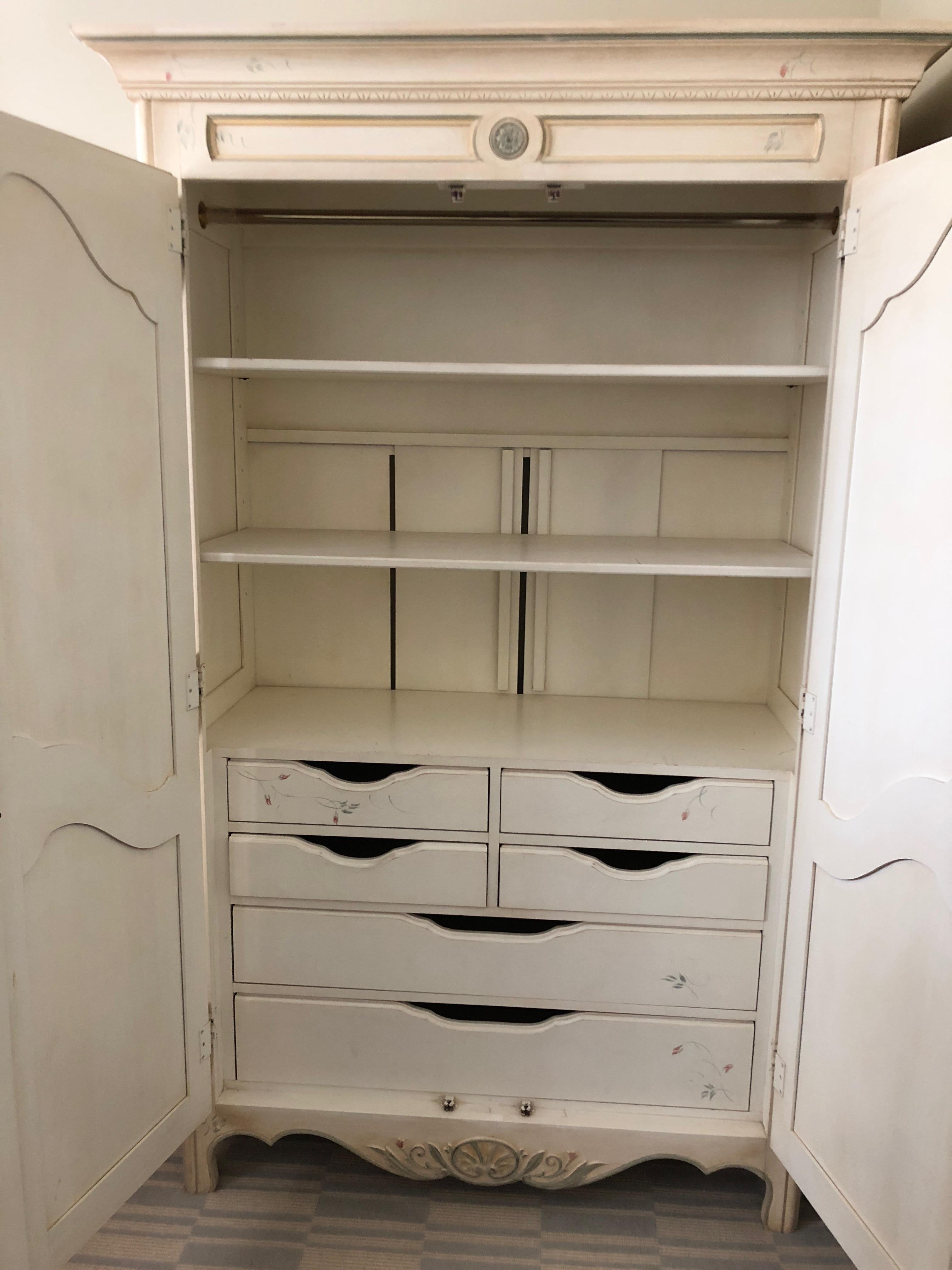 Versatile armoire by Ethan Allen painted with a floral pastel motif against off white background, having drawers inside and a dowel for hanging clothes. The back panels separate to allow electronic equipment wires through for TV or stereo storage.