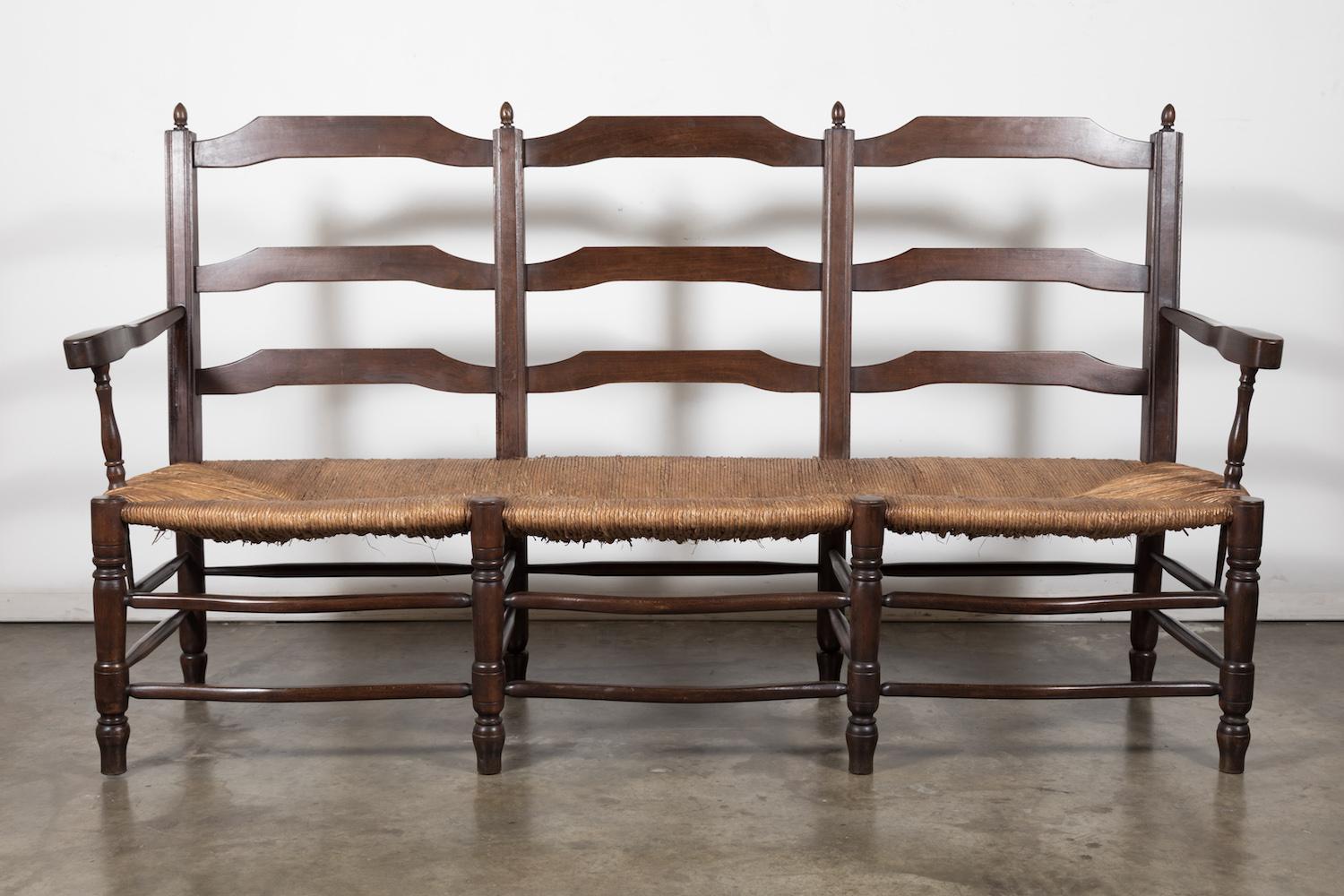 Charming French Country walnut settee or radassier, circa 1930s. This double arm bench from Provence seats three and features a handwoven rush seat and ladder-back. A wonderful rustic look that captures the feeling of rural France. Simple yet