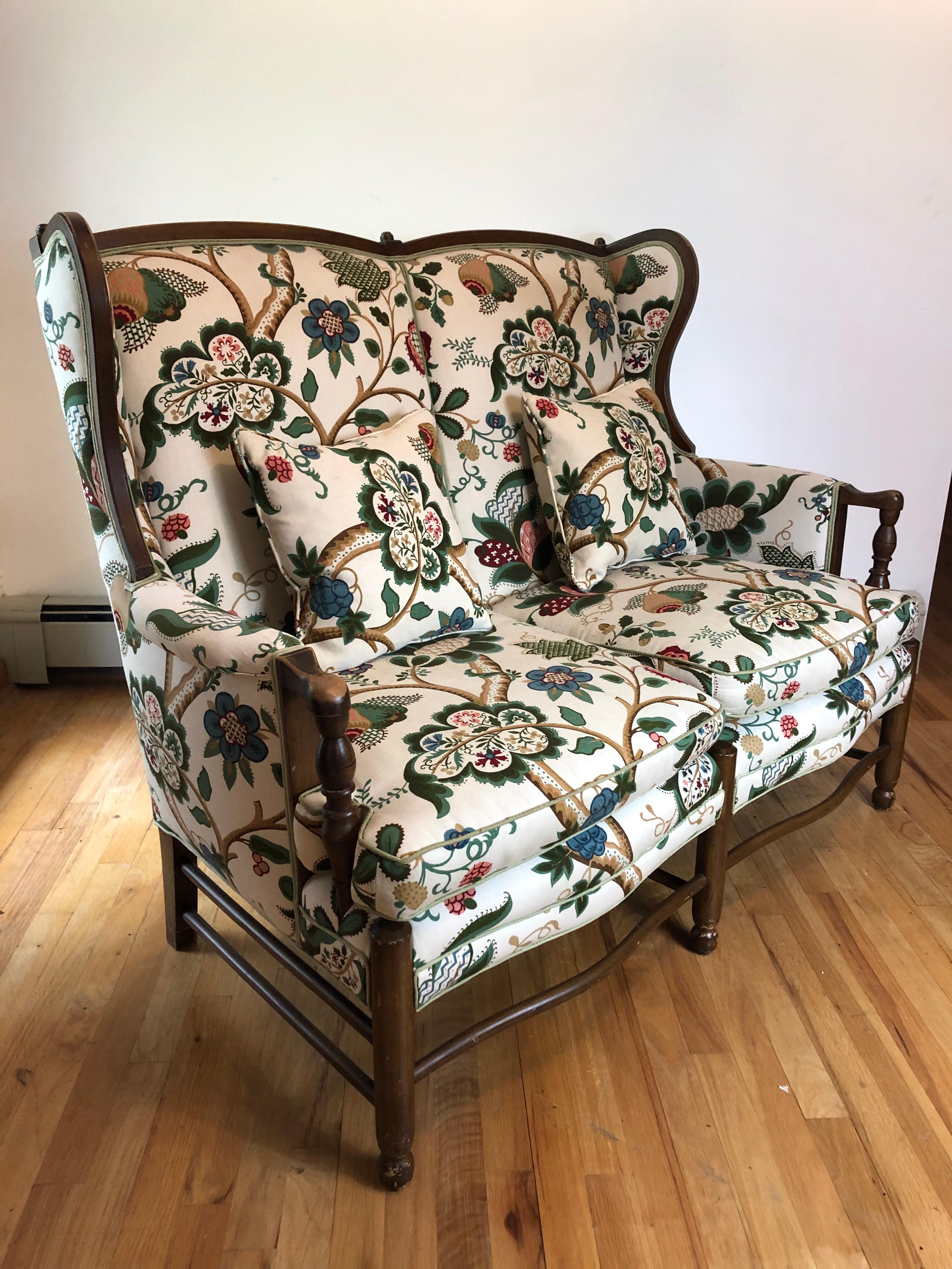 A French country style oak wingback settee with joined stretcher and turned armrests. Floral printed cotton canvas and matching pillows are in excellent condition.