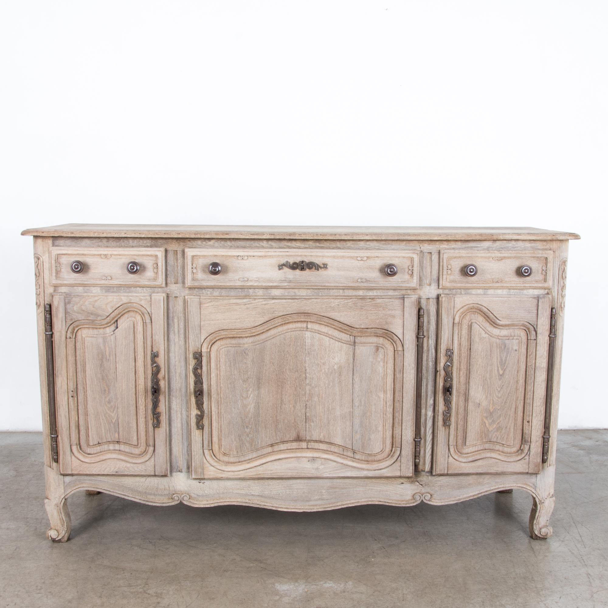 A three-drawer buffet cabinet in bleached oak. From France, circa 1900, this well proportioned provincial oak piece is accentuated by distinctive iron hardware. Decorative floral carvings give a sense of place, the beauty of nature. Attention to