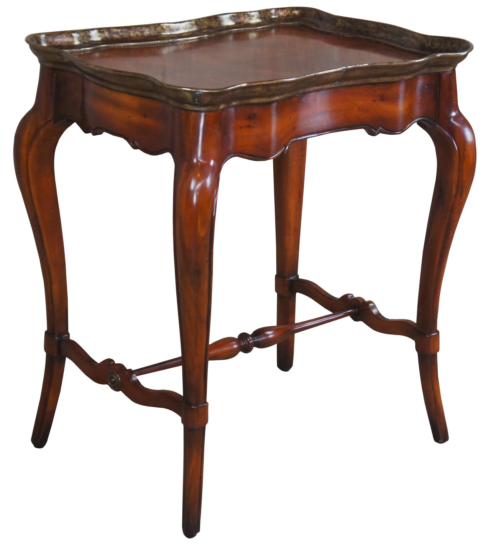 A stunning French inspired accent table. Made from walnut with an inset matchbooked top featuring a patinated brass scalloped edge. The table is supported by long cabriole legs connected by a serpentine H stretcher with brass button and turned
