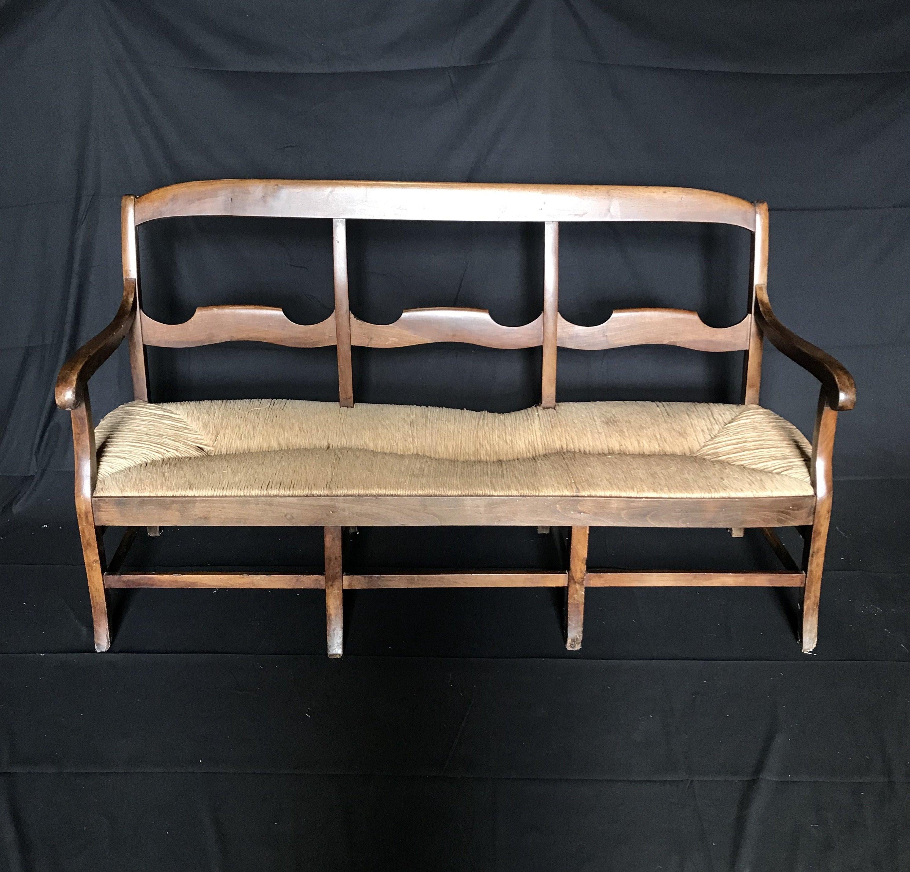 Beautiful, shapely carved antique walnut bench from 19th century France having rush seat with exposed ladder back wooden frame and original rush. Graceful curved arms and subtle cabriole legs. Marvelous color and good natural patina complete the
