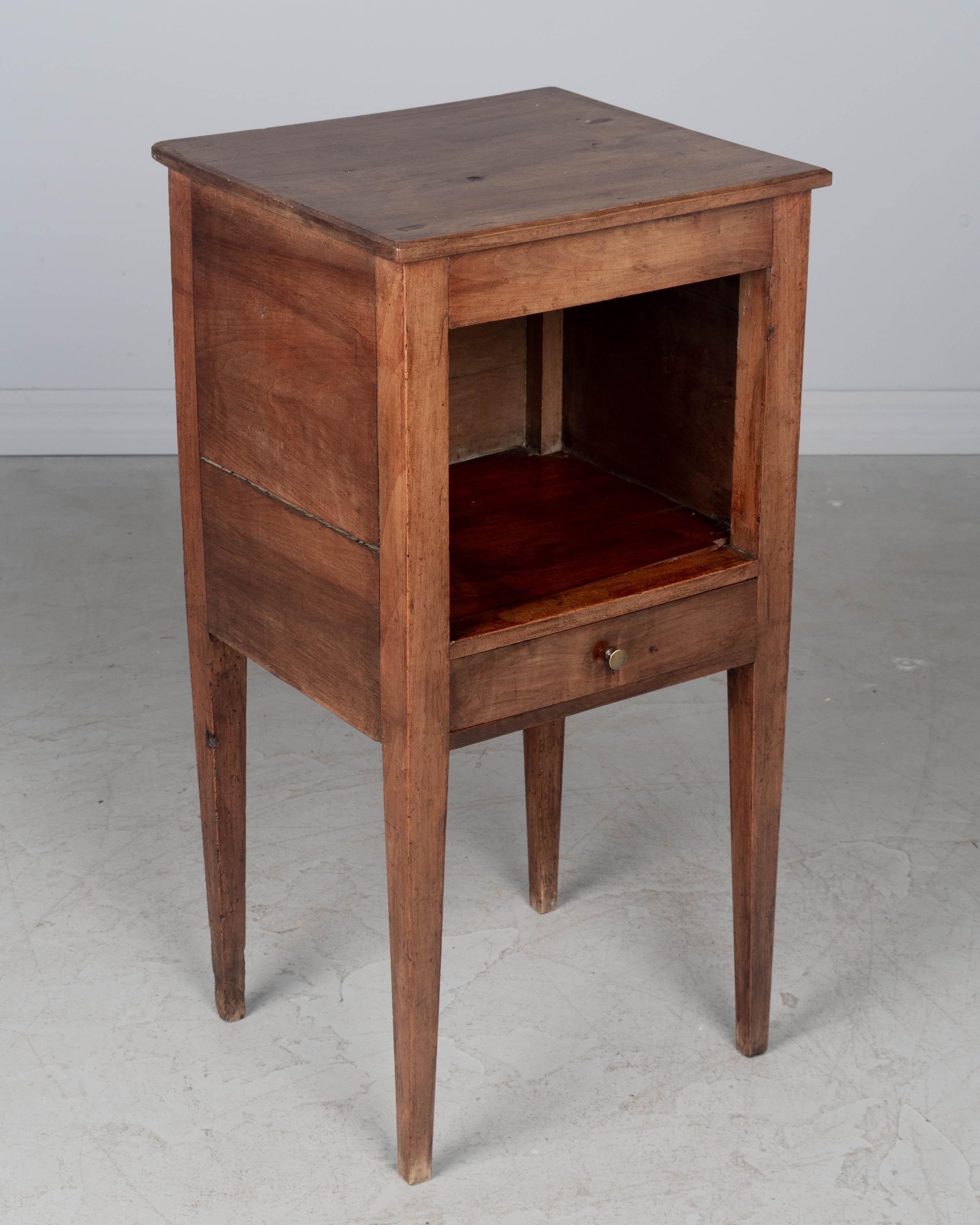 Table d'appoint, ou table de nuit, en noyer massif, du XIXe siècle, avec une niche ouverte et un petit tiroir avec une tirette en laiton. De bonne qualité et de fabrication artisanale, avec des pieds robustes et effilés. Patine cirée. Circa