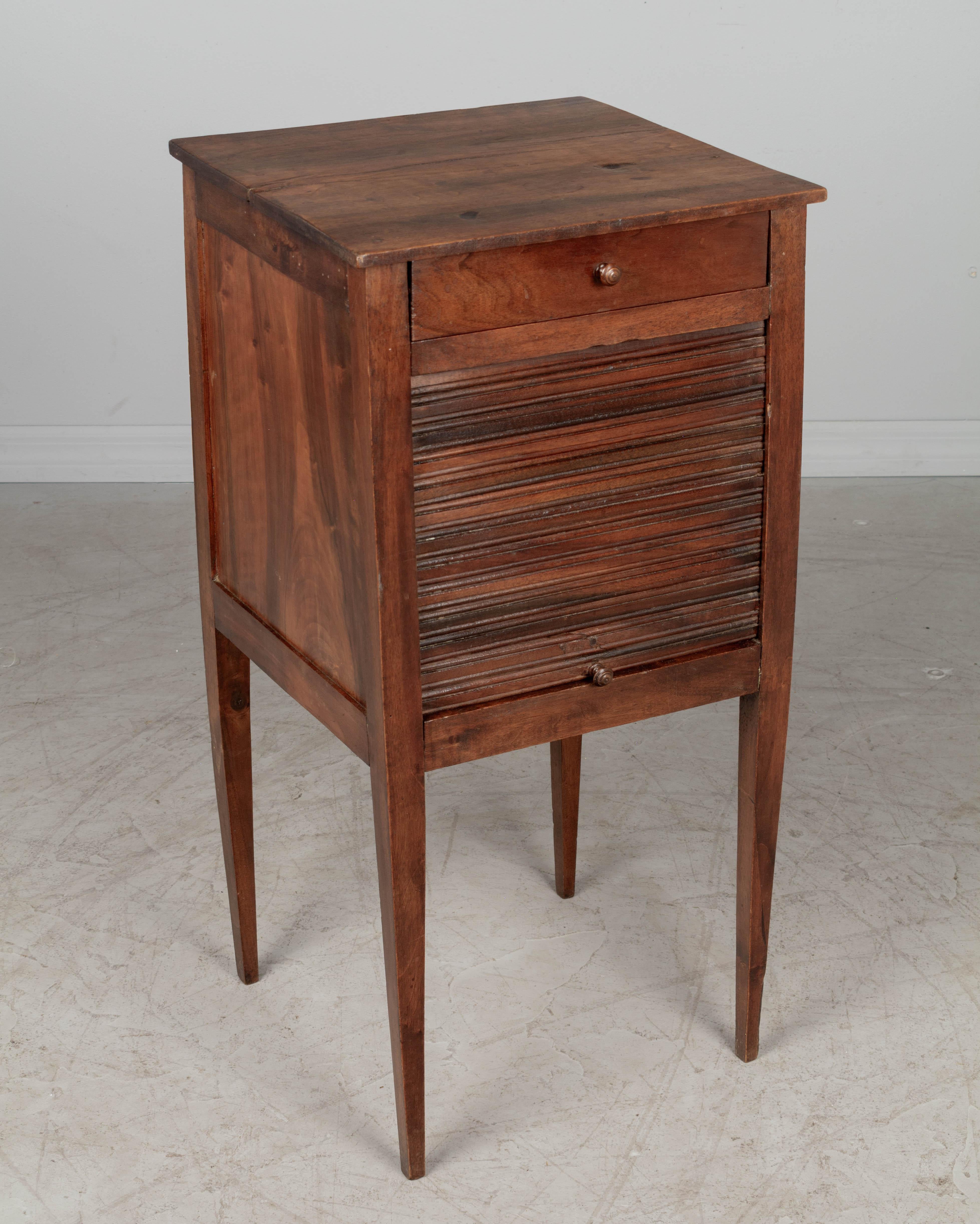 A French Country walnut side table with a vertical tambour door. Finished on all four sides. Slender tapered legs. Waxed patina. All original. May be used as a bedside table. Good overall condition. Circa 1900-1920. 
15.25