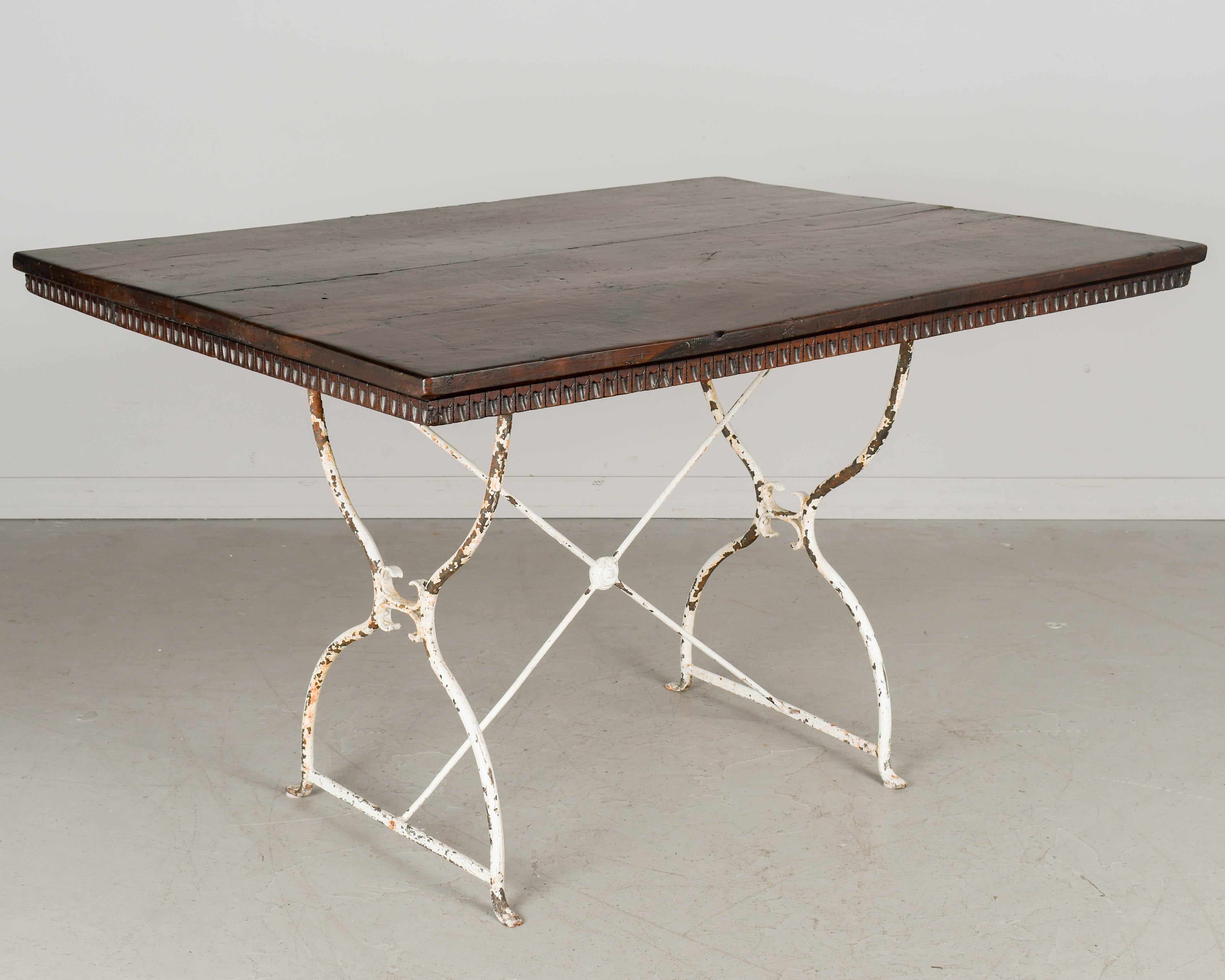 A dining table made with the walnut top from an 18th century Spanish Baroque table and a 19th century white painted wrought iron bistro table base. The top is made of two planks of thick walnut with decorative trim beneath the perimeter and has a
