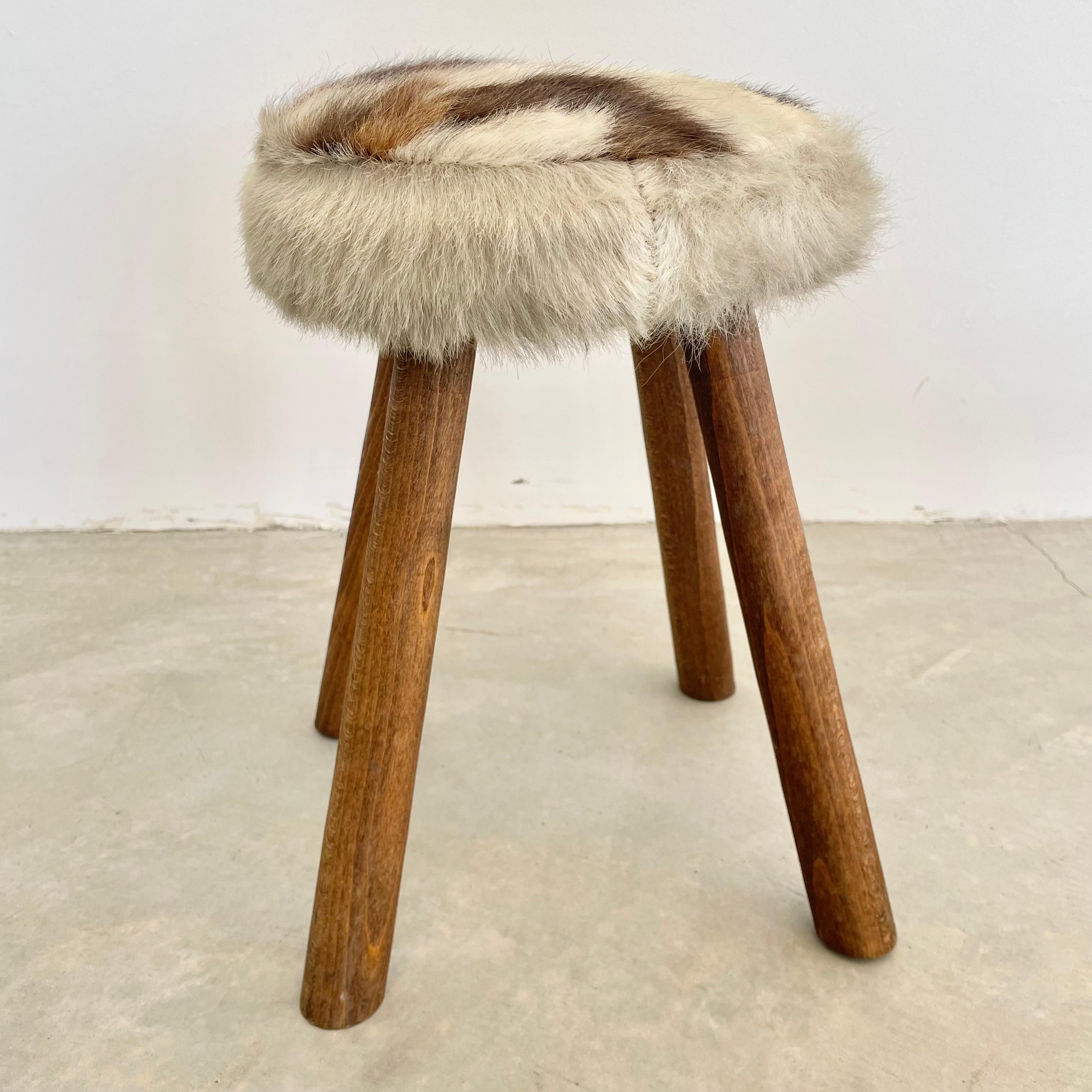 Unique 4 legged stool made in France, circa 1960s. Substantial and chunky round seat covered in a cushion and thick cowhide with spotted fur ranging from cream to tan and brown. Fur still in good condition with some soiling and minimal breakage to