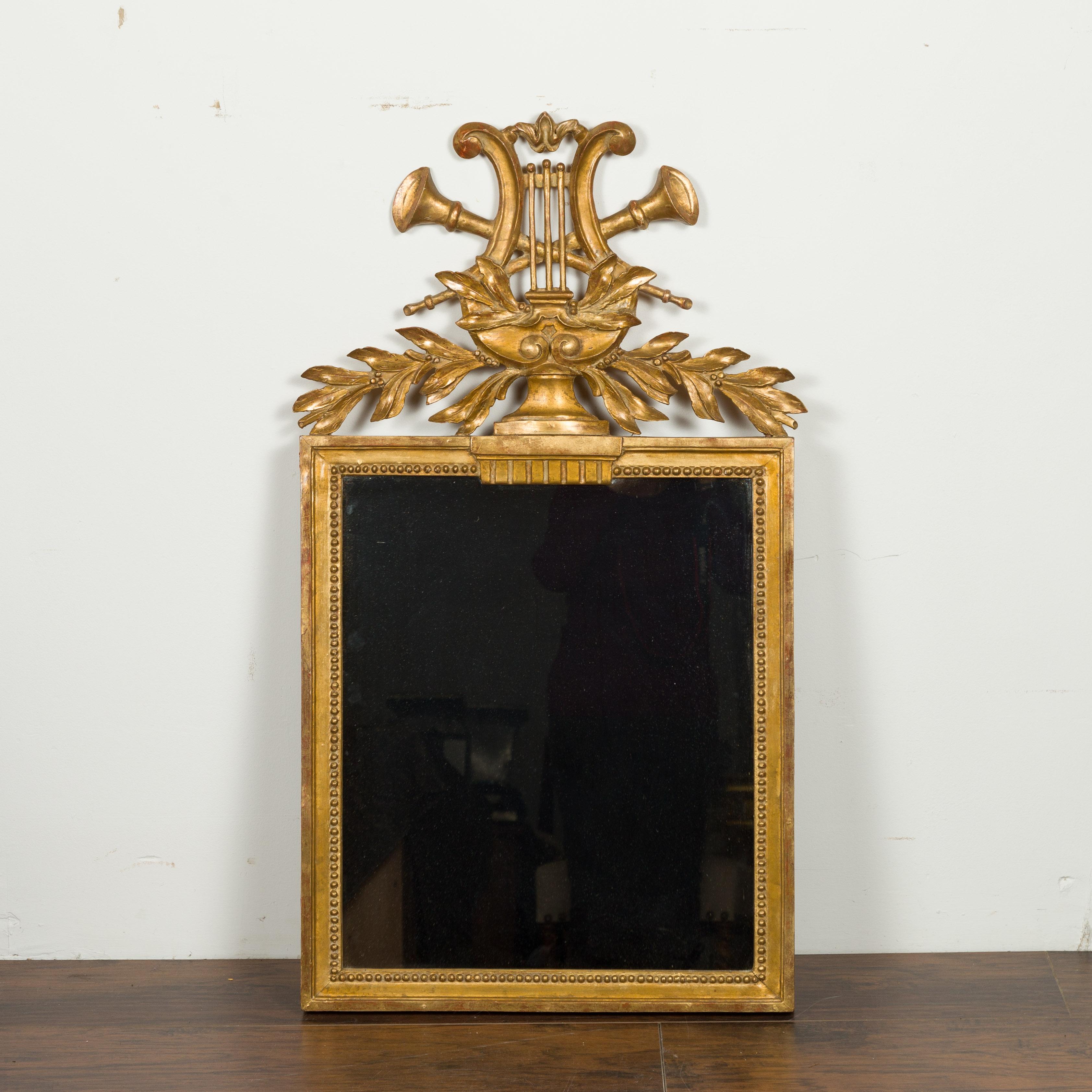 A French giltwood crested mirror from the early 20th century, with carved Music Allegory. Created in France during the early years of the 20th century, this exquisite mirror features a carved lyre and two woodwind instruments. Accented with olive