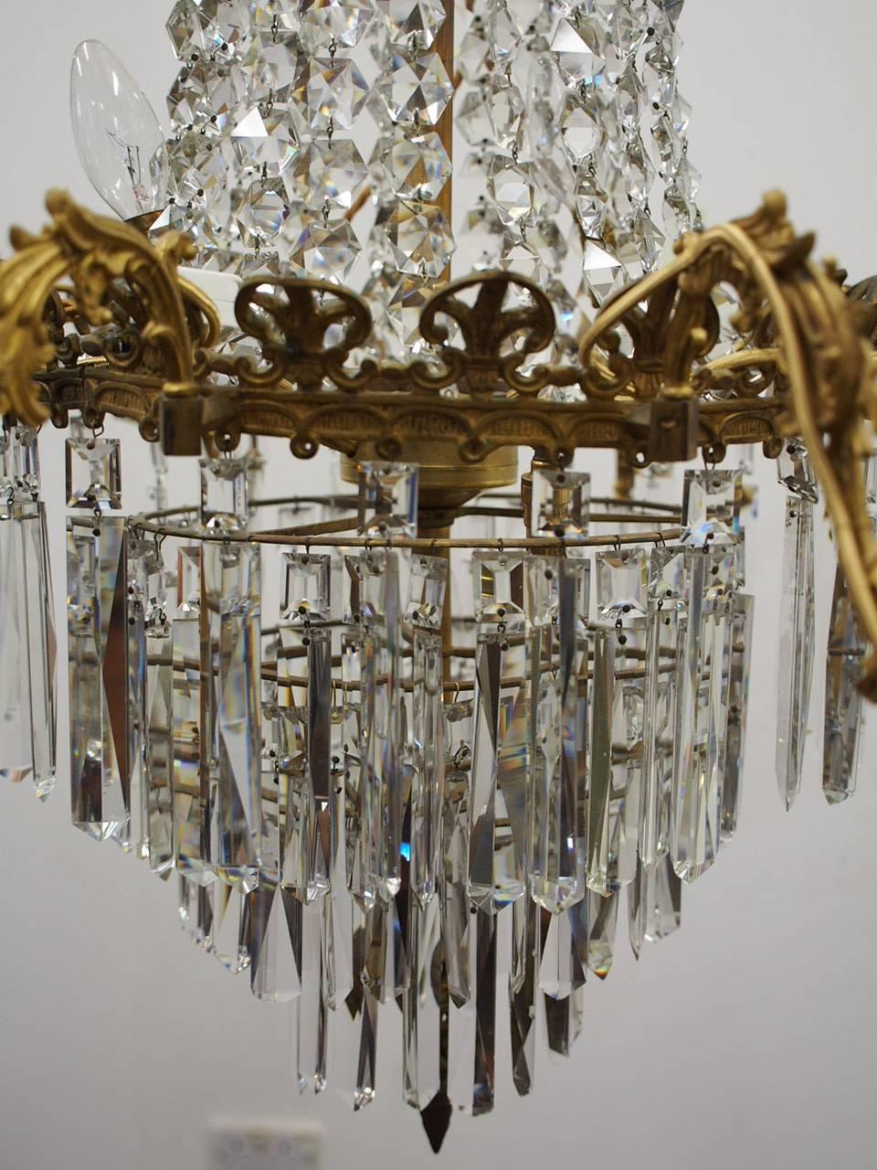 Late Victorian French crystal and gilded brass chandelier, circa 1880. The tent form top has a stylish foliate circular pediment. Beneath this, the first bezel carries several strands of faceted glass which taper down to the next section, and