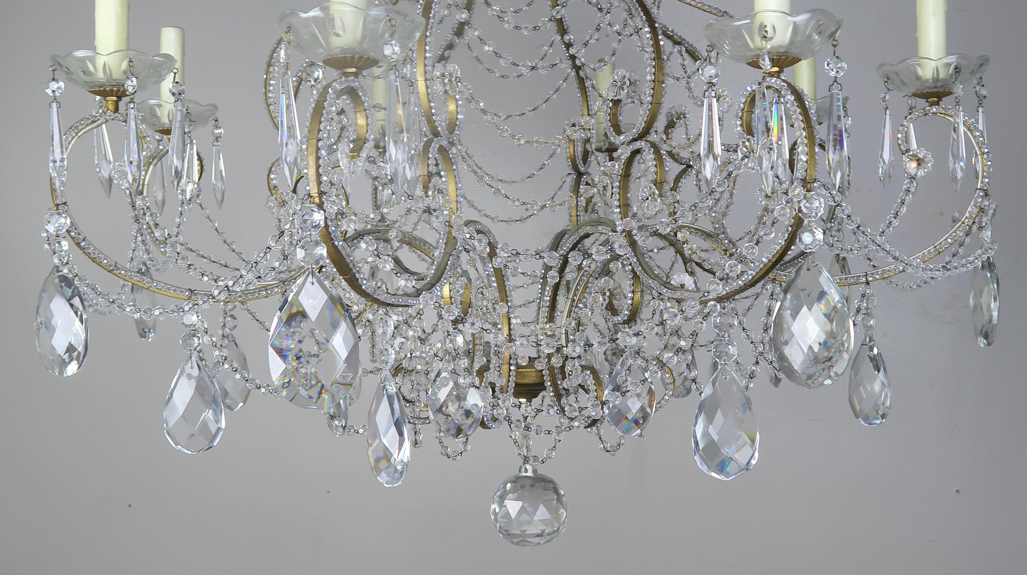 Lampadario a 8 bracci in cristallo francese con cristalli sfaccettati a forma di mandorla. L'apparecchio è inoltre ornato da ghirlande di perline inglesi. L'apparecchio è stato ricablato di recente con coperture per candele in cera a goccia color