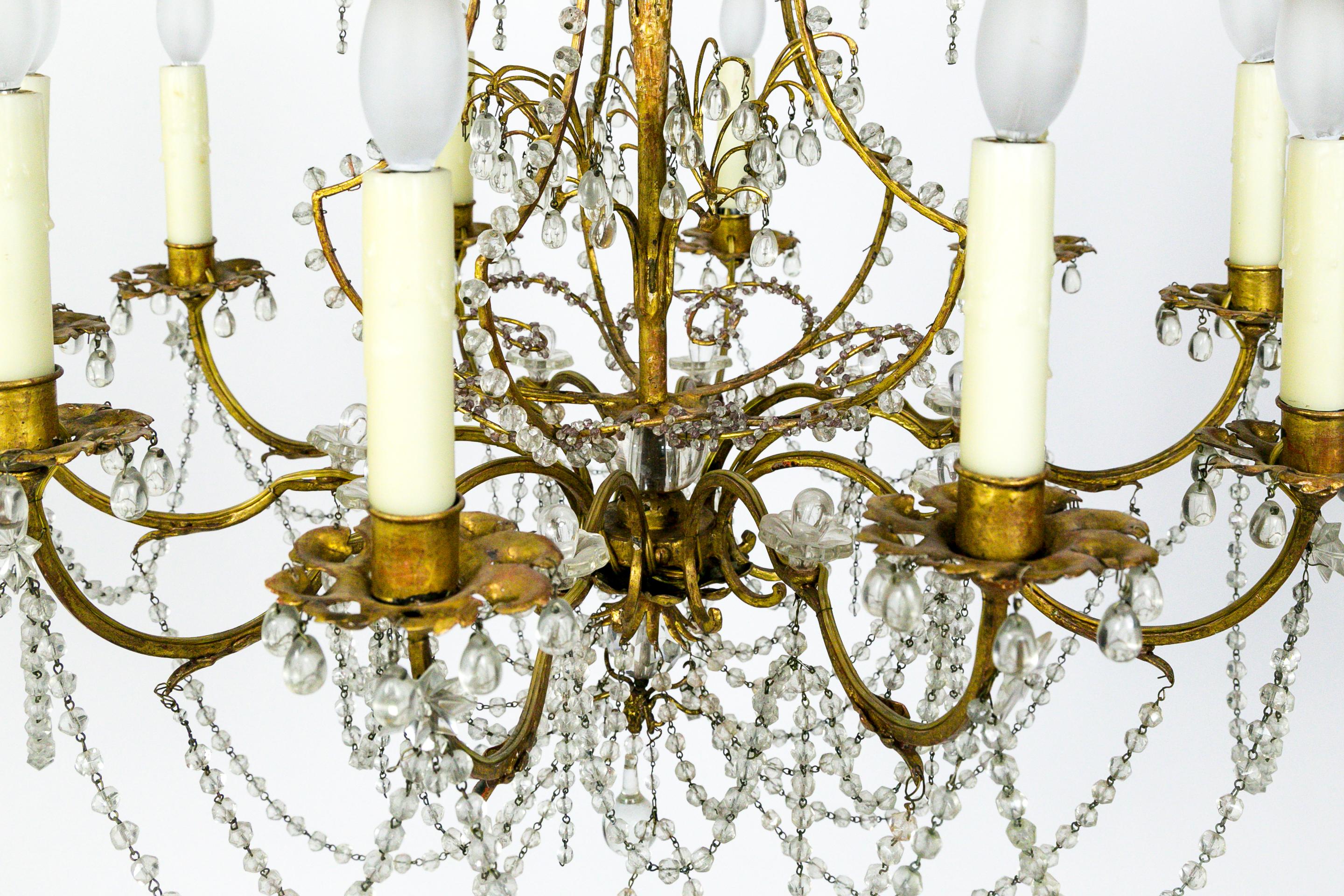 This ornate, crystal beaded, 10-light chandelier has gorgeous, bead encrusted, brass curls and scrolls. Small, lavender crystals accent the curling shapes at the top, along with various shaped crystals throughout the rest of the body. The brass has