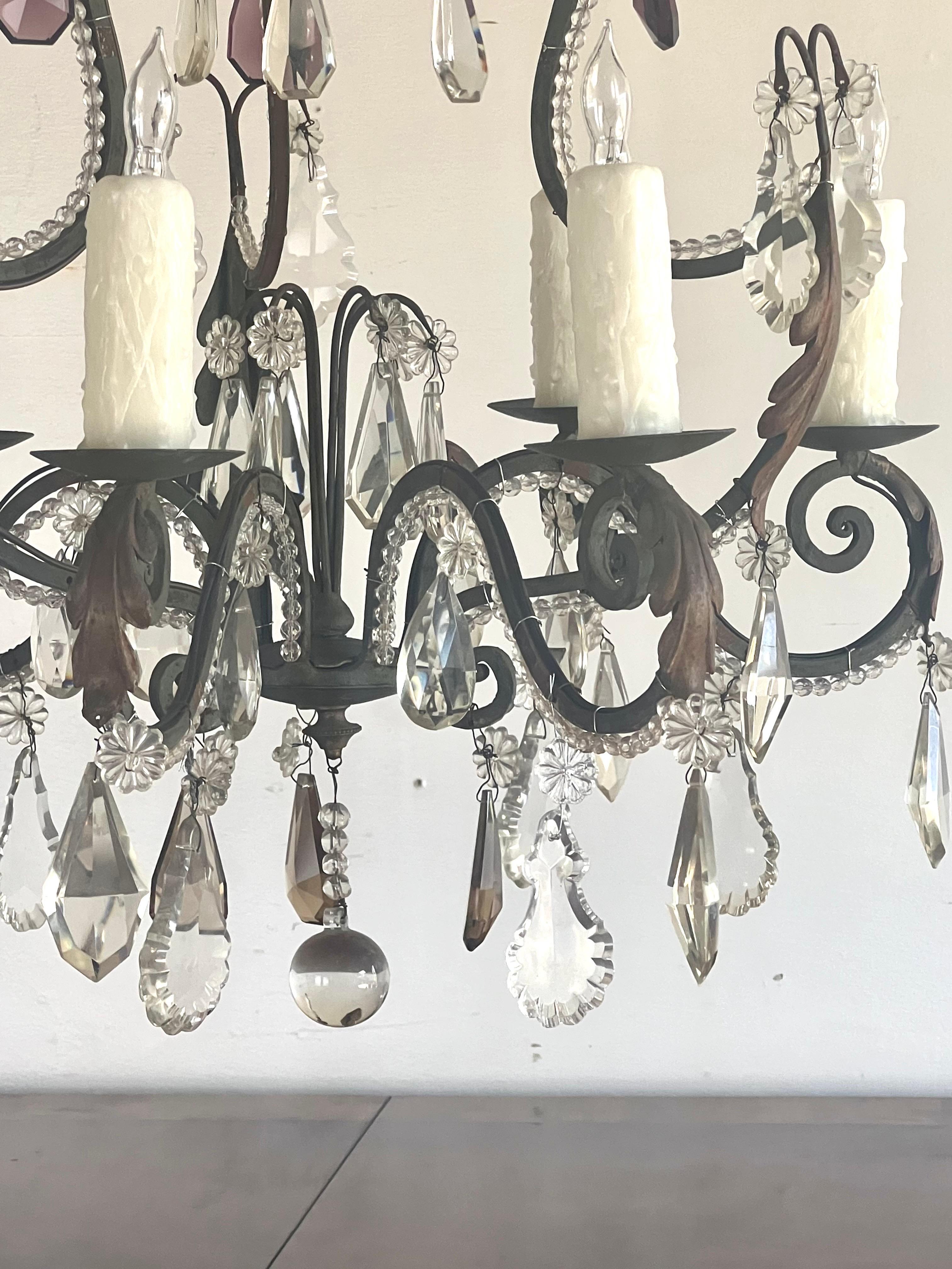 Lampadario francese ornato in ferro e cristallo dal design classico.  I bracci ornati a spirale, le luci a candela e l'abbondanza di prismi di cristallo sono un design influenzato dai lampadari francesi del XVIII e XIX secolo.  I lampadari francesi,