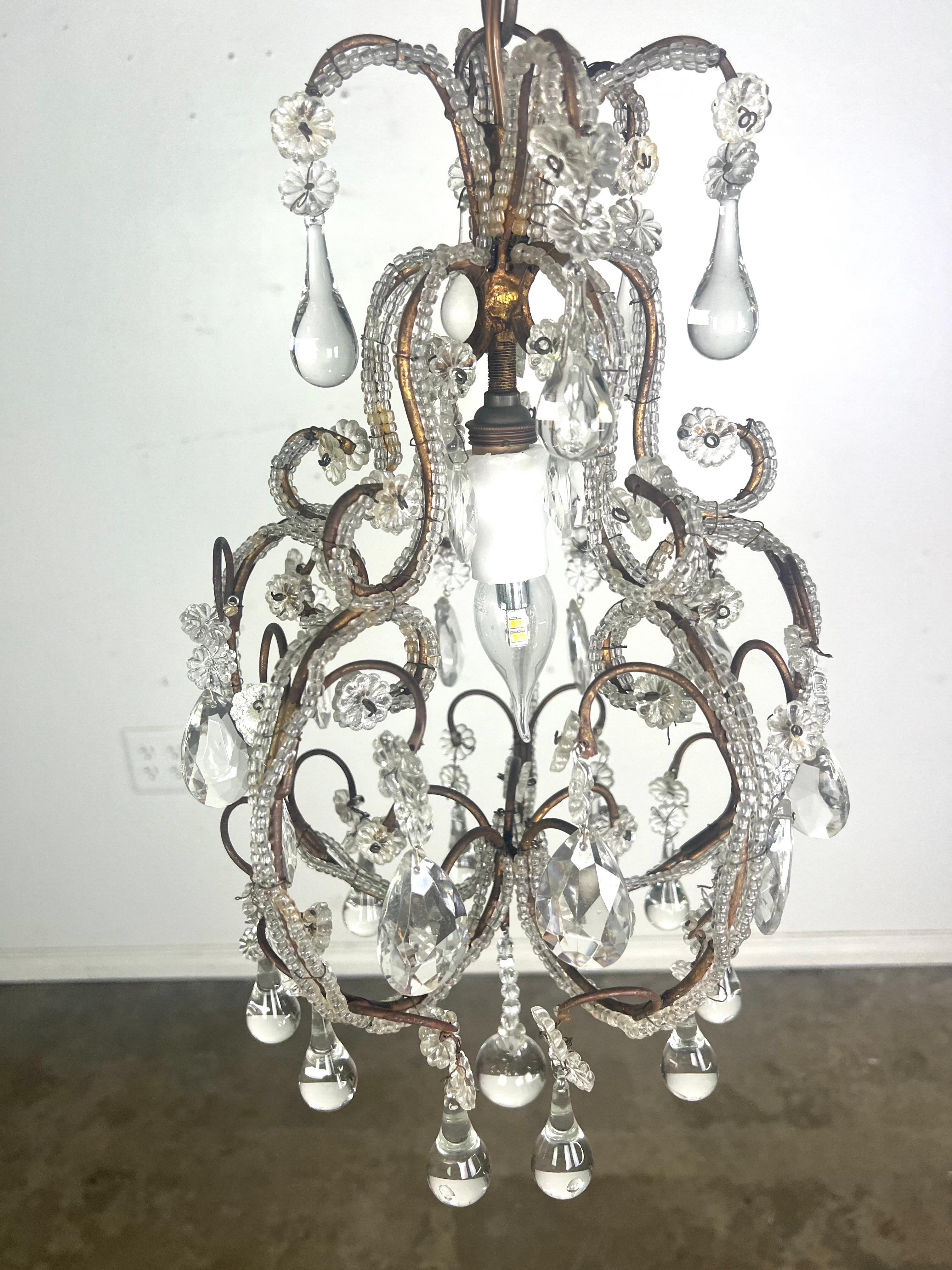Il lampadario è composto da elementi in metallo e cristallo.  Ha un design intricato con bracci metallici a scorrimento multiplo ornati da perline e gocce di cristallo.  I cristalli sono un mix di forme a goccia e floreali, che catturano e
