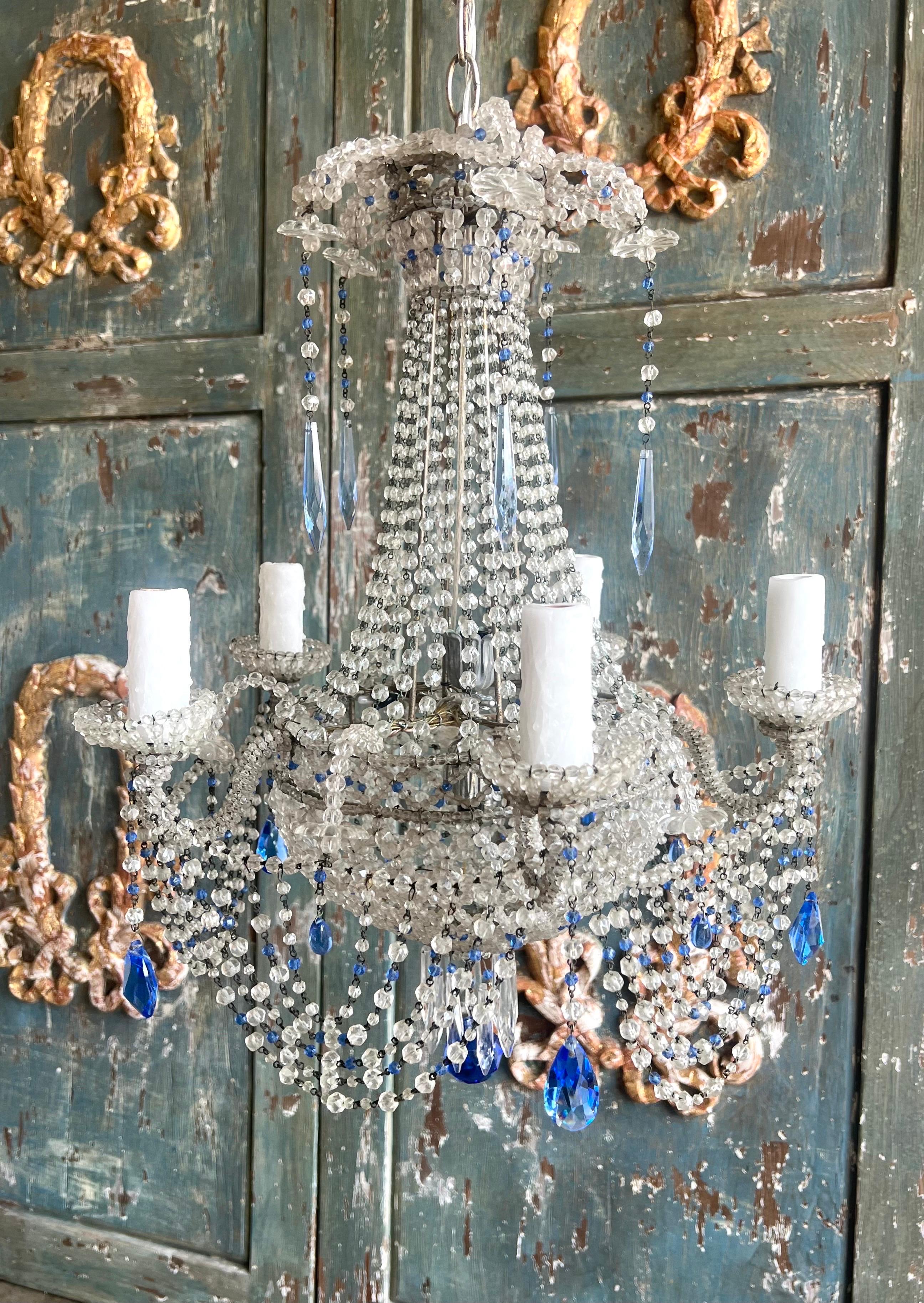 Lampadario a cinque luci in cristallo francese ornato da un'intricata composizione di cristalli chiari e blu.  Presenta una struttura centrale da cui partono diversi fili di piccole perle di cristallo trasparente che scendono verso il basso, creando