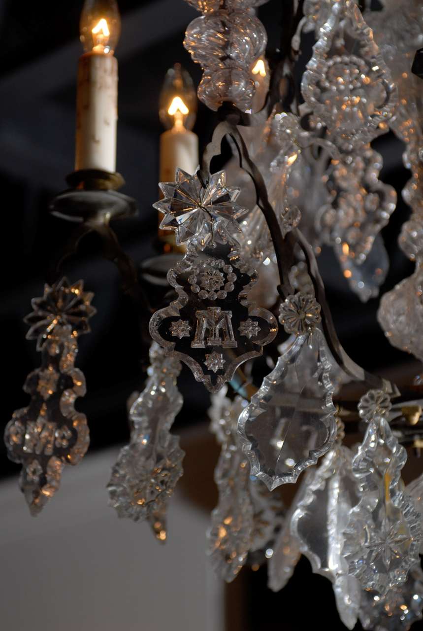 A French Baroque Revival crystal six-light chandelier from the mid 19th century, with black patinated bronze armature, pendeloques, rosettes and monograms. Found in a French church, this exquisite crystal nine-arm chandelier features a central