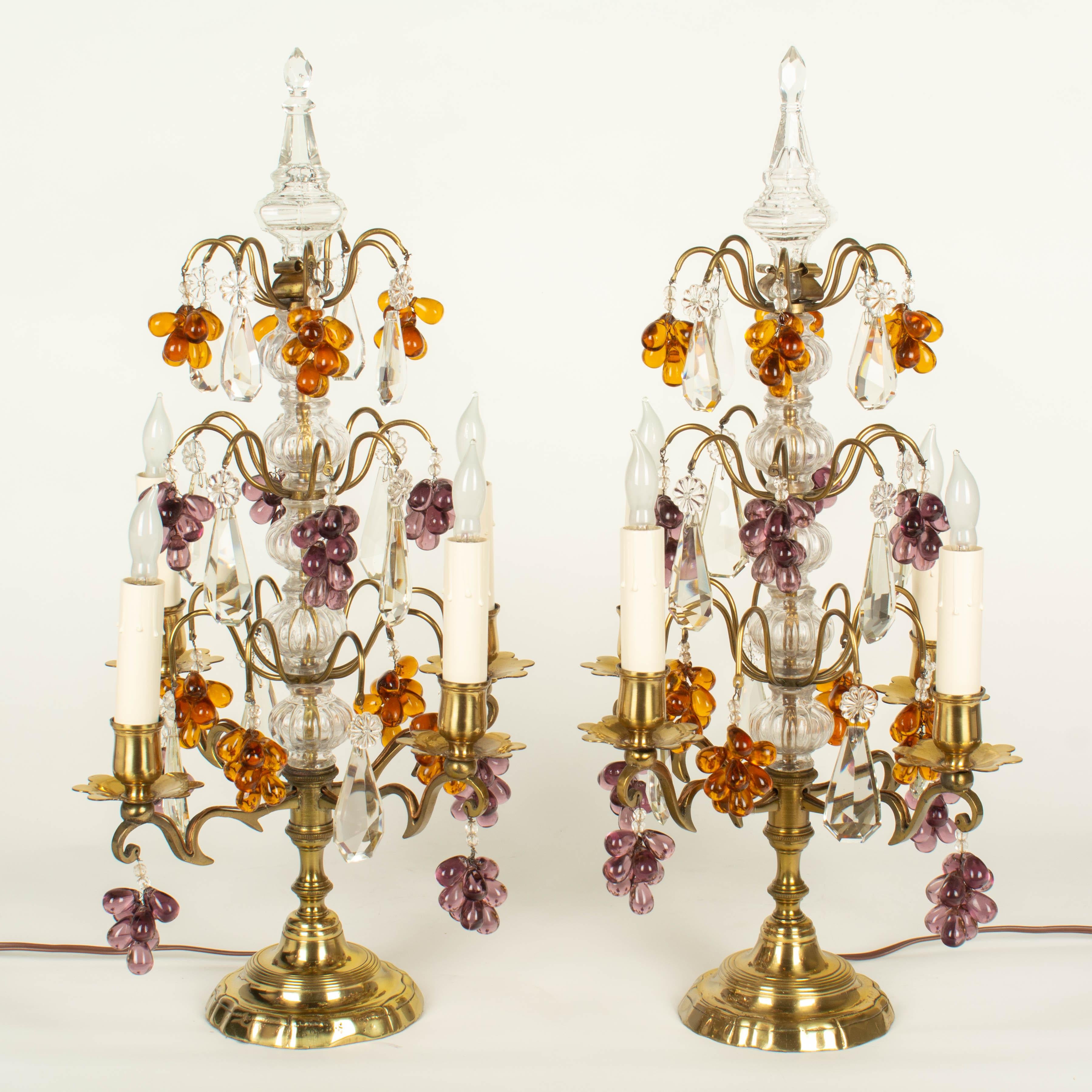 A pair of Louis XV style four-light French girandoles, or chandelier table lamps. Made of polished brass with three tiers of bevel cut crystal prisms and amber and amethyst grape clusters, ribbed columns and spear finials. Tall, elegant proportions.