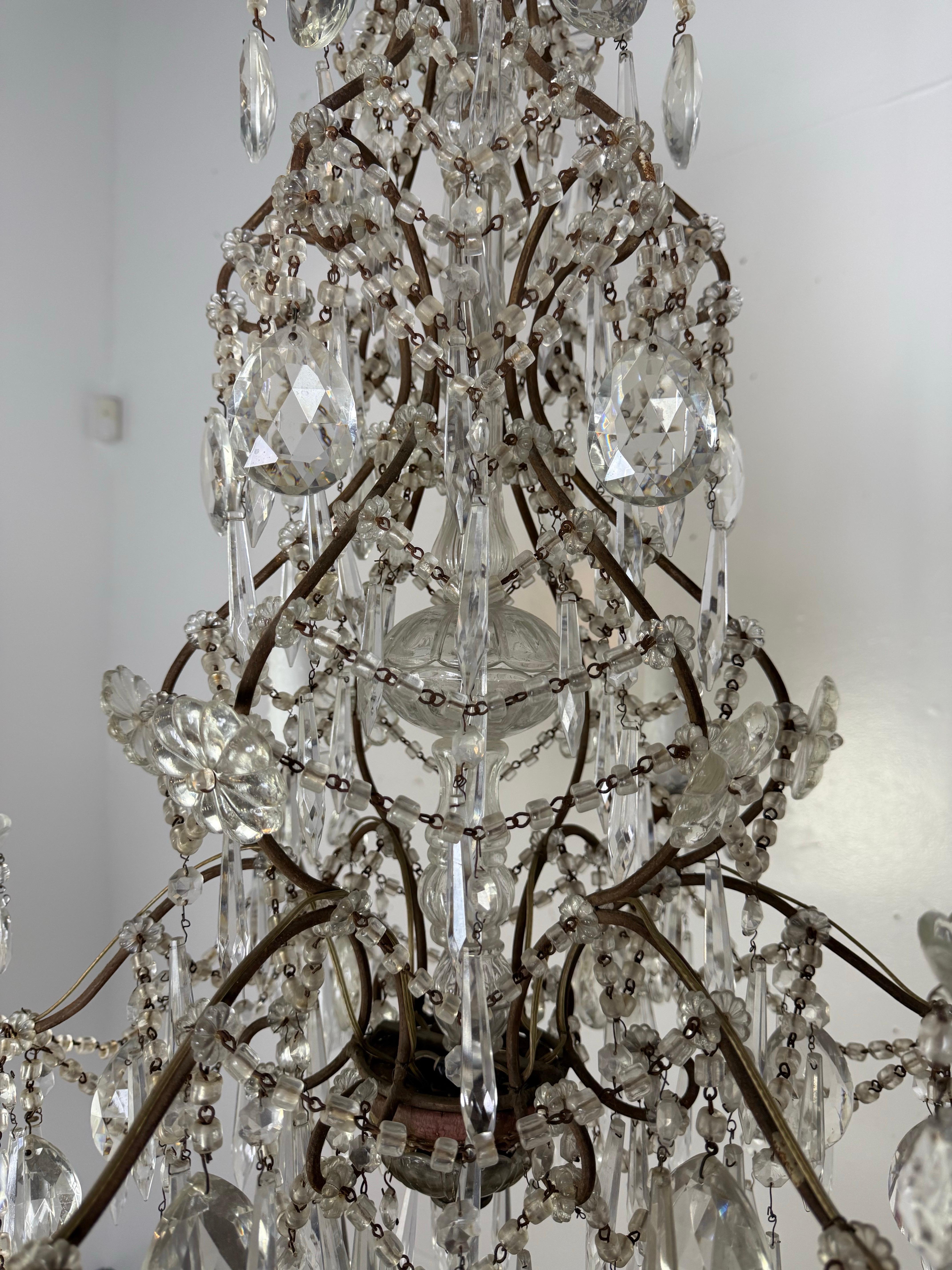 Questo squisito lampadario di cristallo antico è un raffinato esempio di artigianato europeo dell'inizio del XX secolo, caratterizzato da una cornice ornata da delicate perline di maccheroni e da un'abbagliante serie di gocce e festoni di cristallo