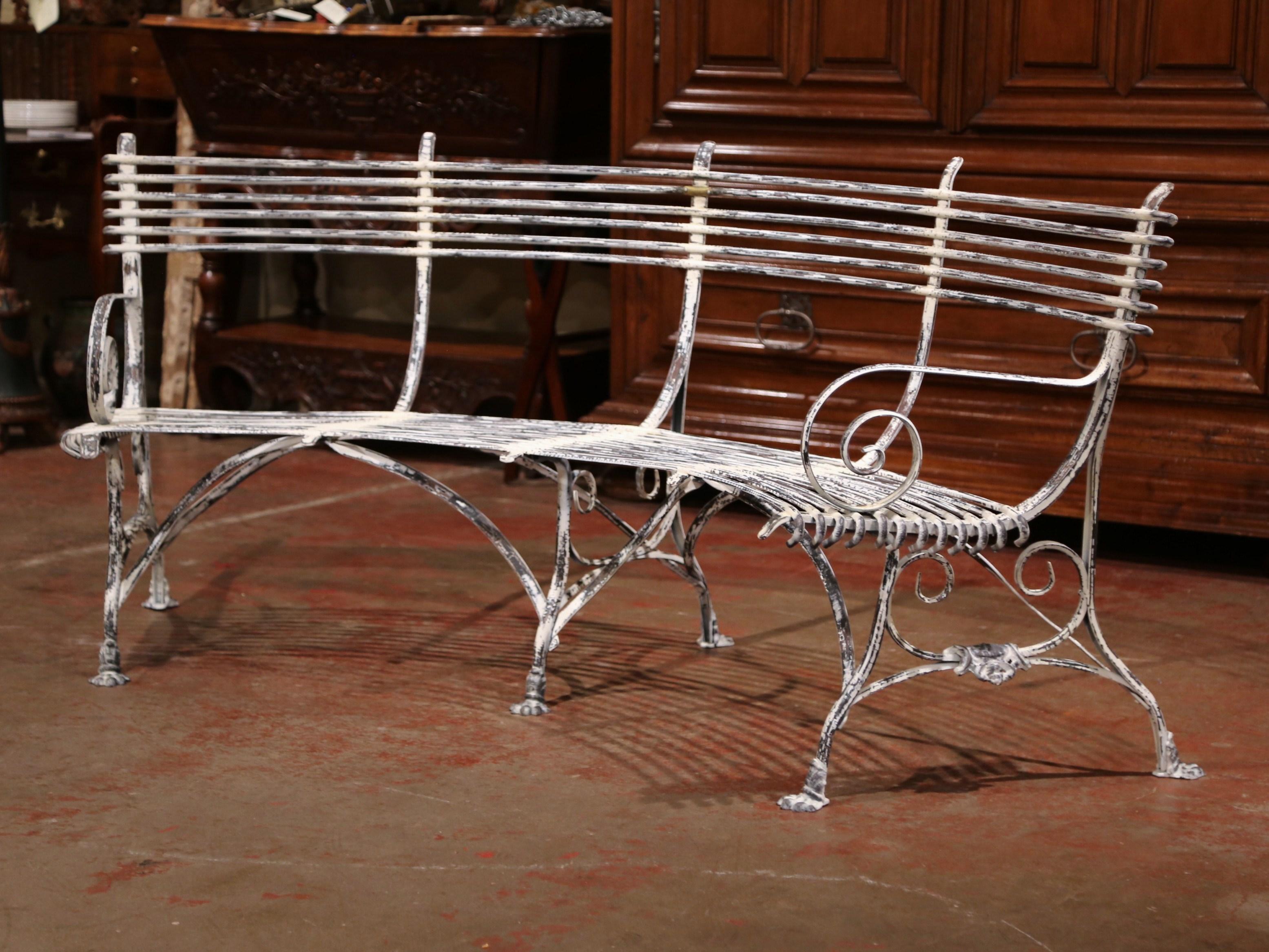 This elegant forged and curved iron bench was crafted in France. The rounded bench has gracious lines, scrolled armrests, a curved back and six paw feet connected with stretchers; the seating has a antique white patinated paint finish. The bench is