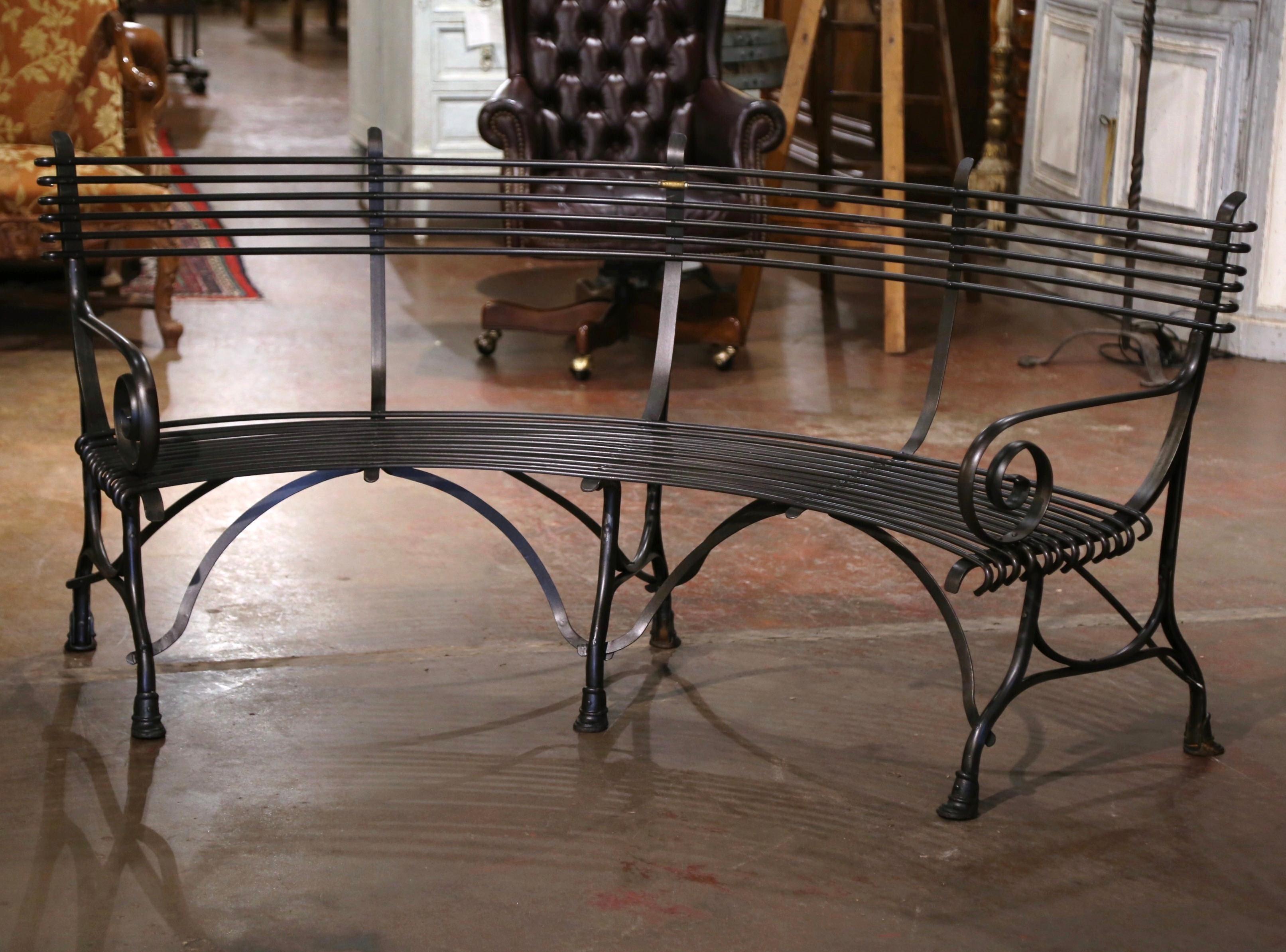 Crafted in France, this elegant forged iron curved bench stands on six legs ending with hoof feet and connected with stretchers at the base. The seating has gracious lines, scrolled armrests, and a curved back; the comfortable four-seat bench is