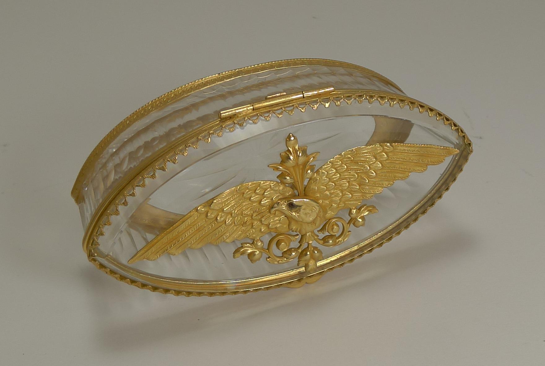 A most unusual and highly collectable cut crystal box of oval form with elegant channel cuts all around the sides.

The fittings are all made from gilded bronze and the lid adorned with a striking eagle with wings spread and the original red stone