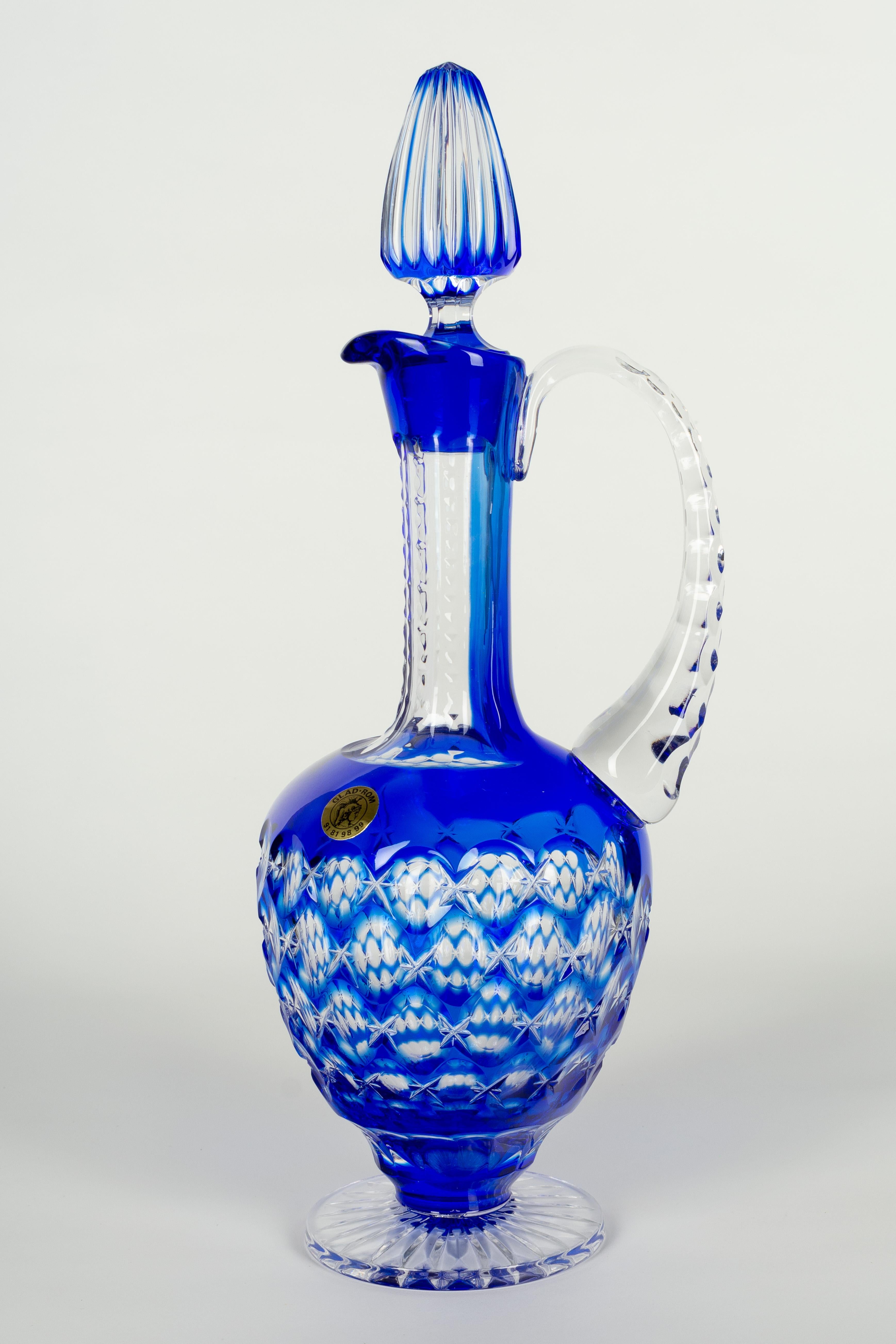 A French cut crystal decanter with stopper, with an outer layer of bright cobalt blue, cut to clear. This ewer shaped pitcher has an elongated neck, clear handle and pedestal base. Original gold foil label reads: GLAD-ROM. 