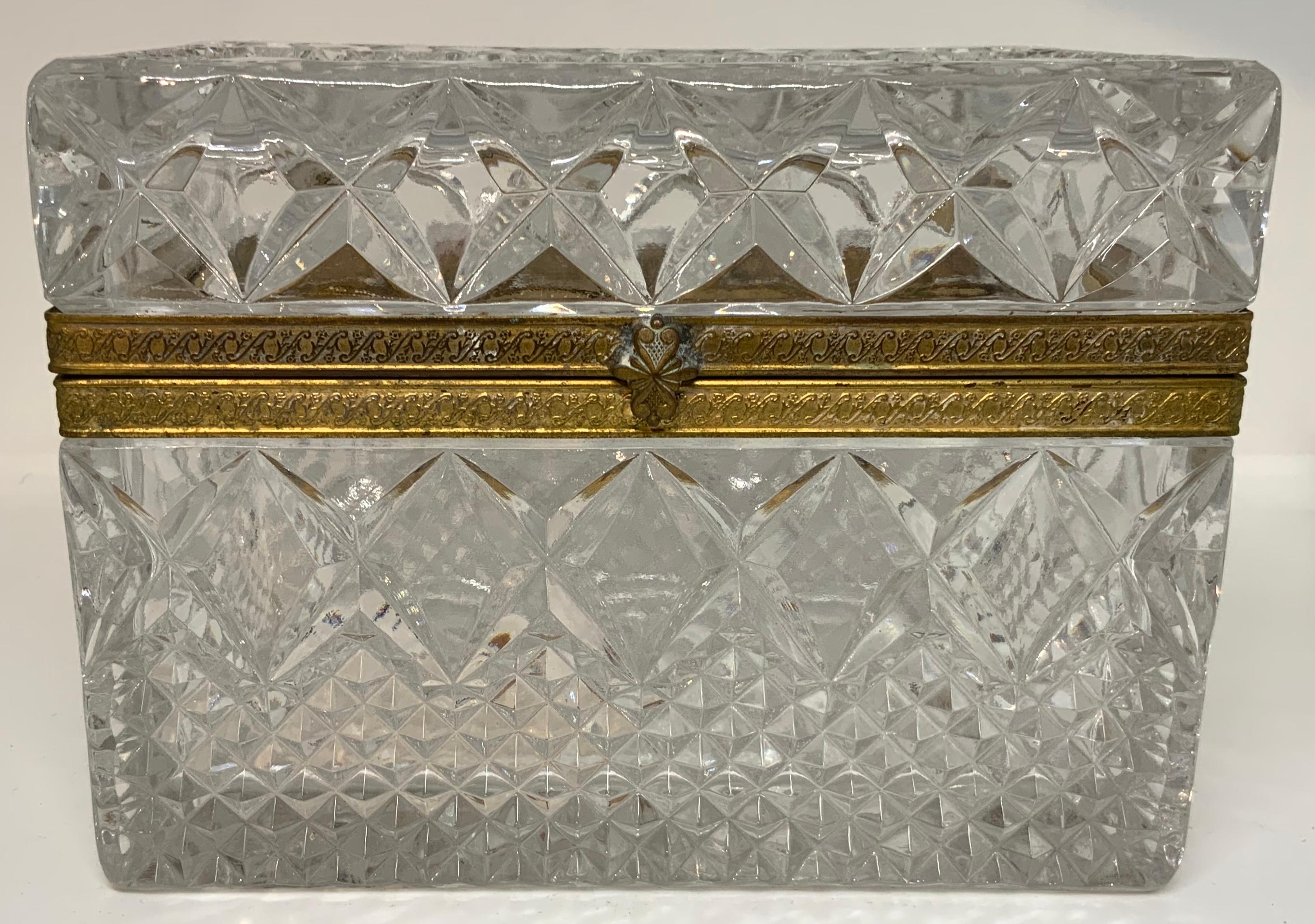 A large rectangular clear cut crystal box with small diamonds cut pattern in the center and bordered by large stars. A starburst is at the bottom. A gilt metal embossed with flowers and scrolls border the hinged lid and the upper top. A double